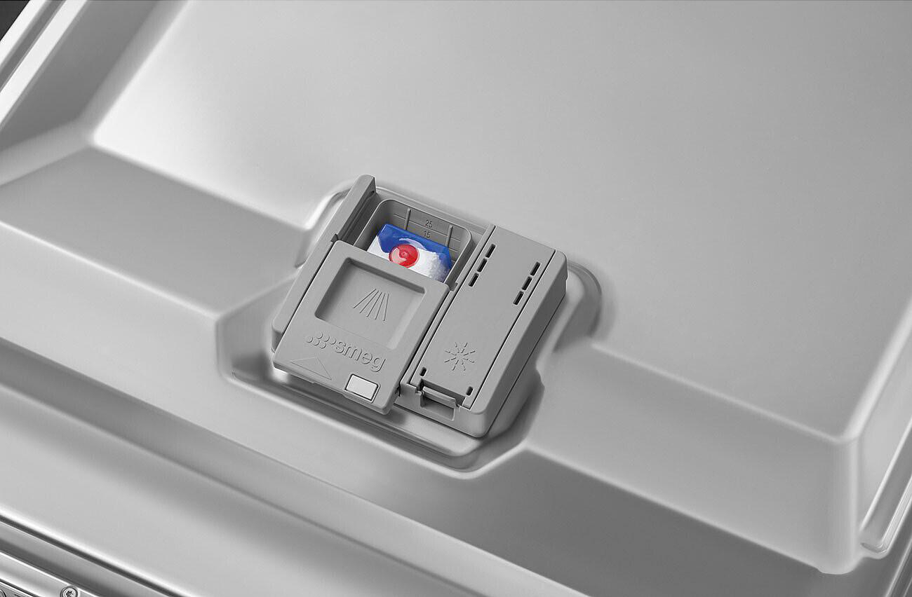 Geschirrspülmittelspender mit einem Reinigungsmittel-Pod. Grauer Smeg-Geschirrspüler-Innenraum. Der Spender ist offen und zeigt das Pod innen.