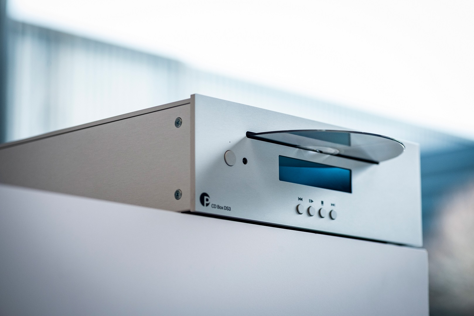 Ein silberner CD-Player mit teilweise eingelegter Disc. Er hat ein blaues Display und Steuertasten. Der Hintergrund ist unscharf.