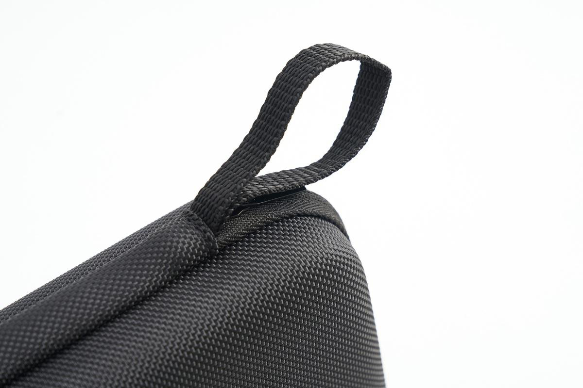 Nahaufnahme eines schwarzen Stoffobjekts mit Schlaufengriff vor weißem Hintergrund. Der Stoff hat ein strukturiertes Muster.