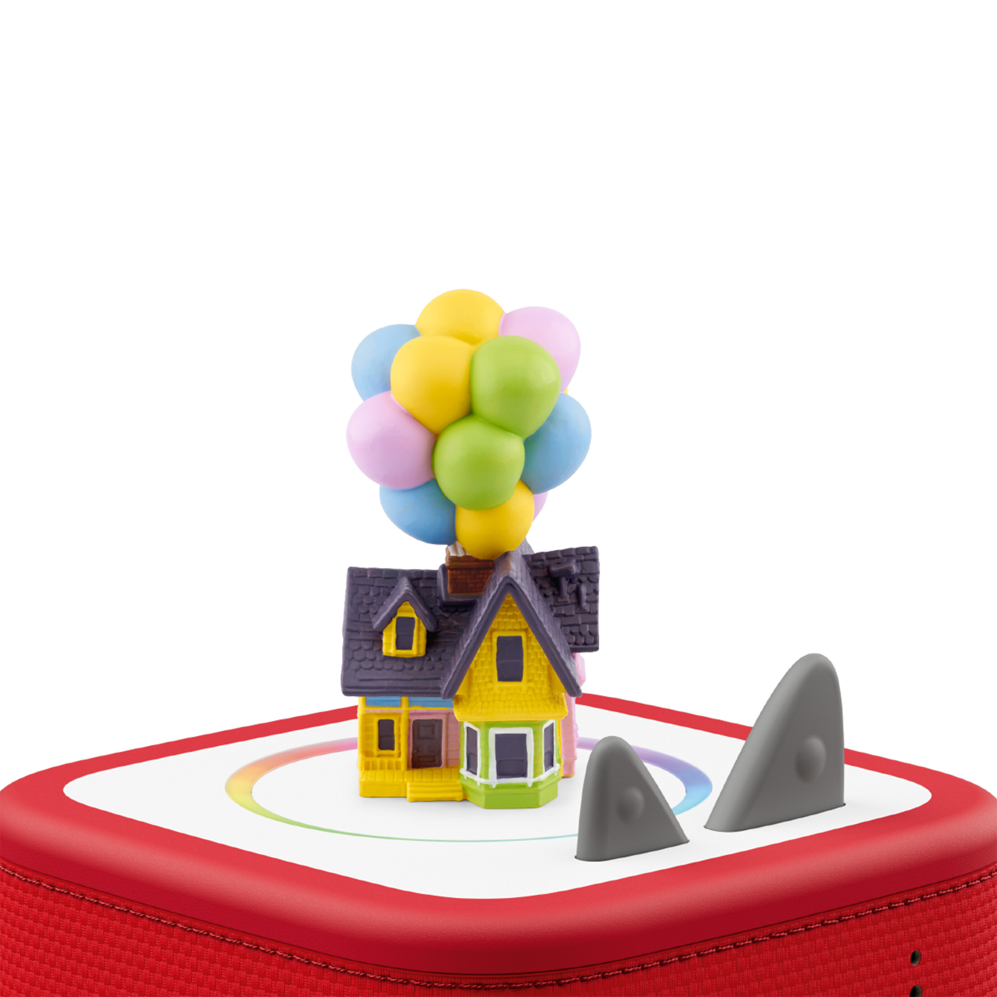 Spielzeughaus mit Ballons auf roter Basis mit grauen Haifischflossen. Haus ist gelb, grün, lila und rosa.