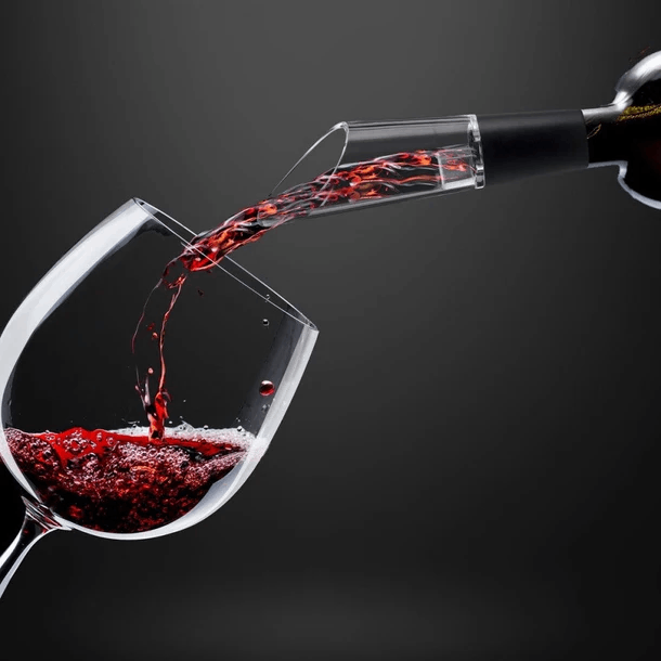 Vino tinto se vierte de una botella a través de un aireador en una copa de vino. Fondo oscuro. Aireador y copa son claros.