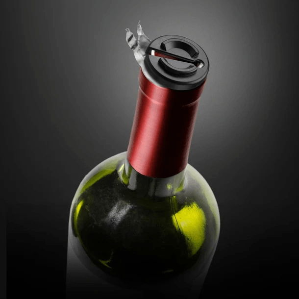 Una botella de vino con un dispositivo negro y plateado en la parte superior. La botella es verde con una etiqueta roja. El fondo es gris oscuro.