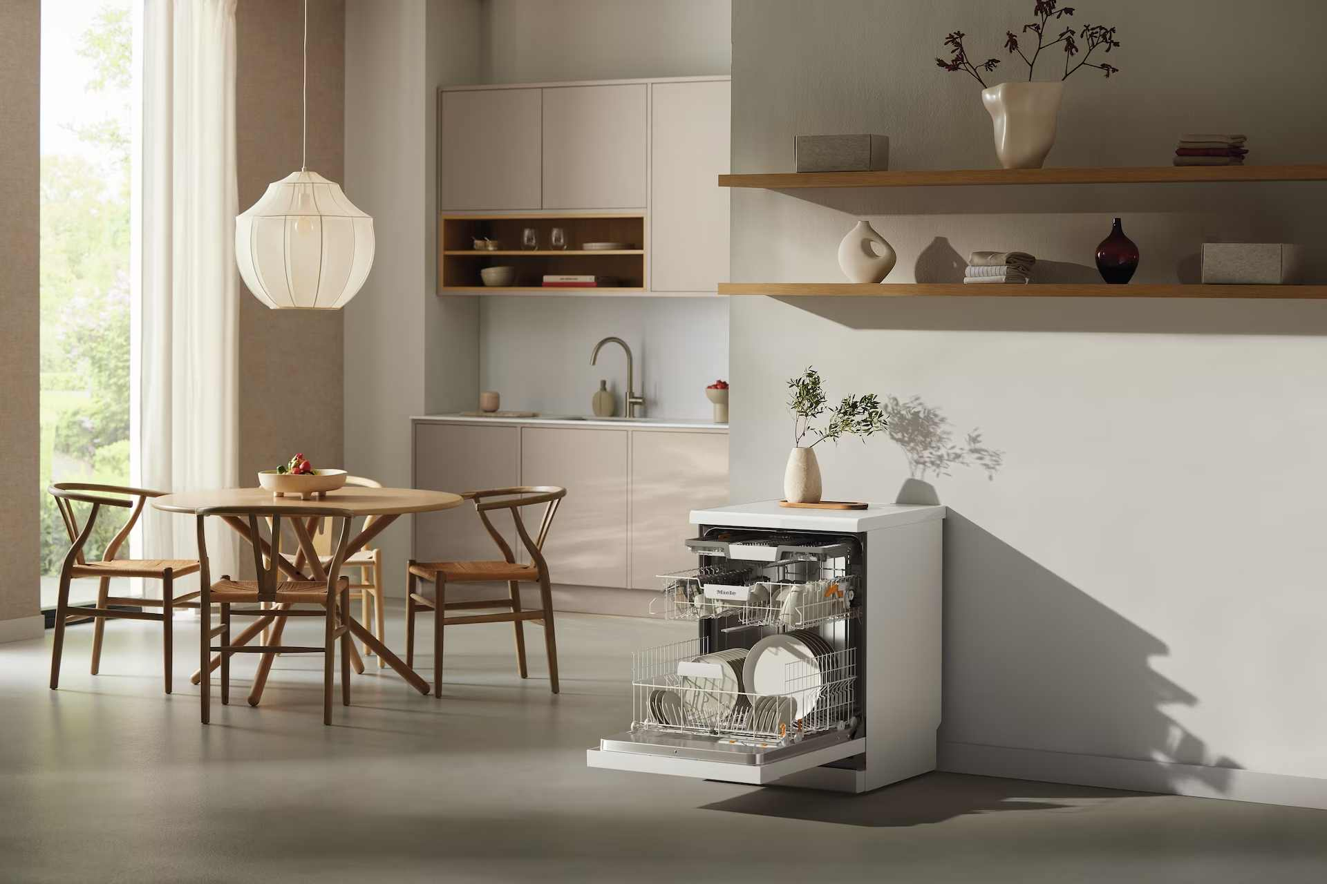 Una cocina moderna con lavavajillas abierto, mesa de comedor con sillas y lámpara colgante. Colores neutros y luz natural.