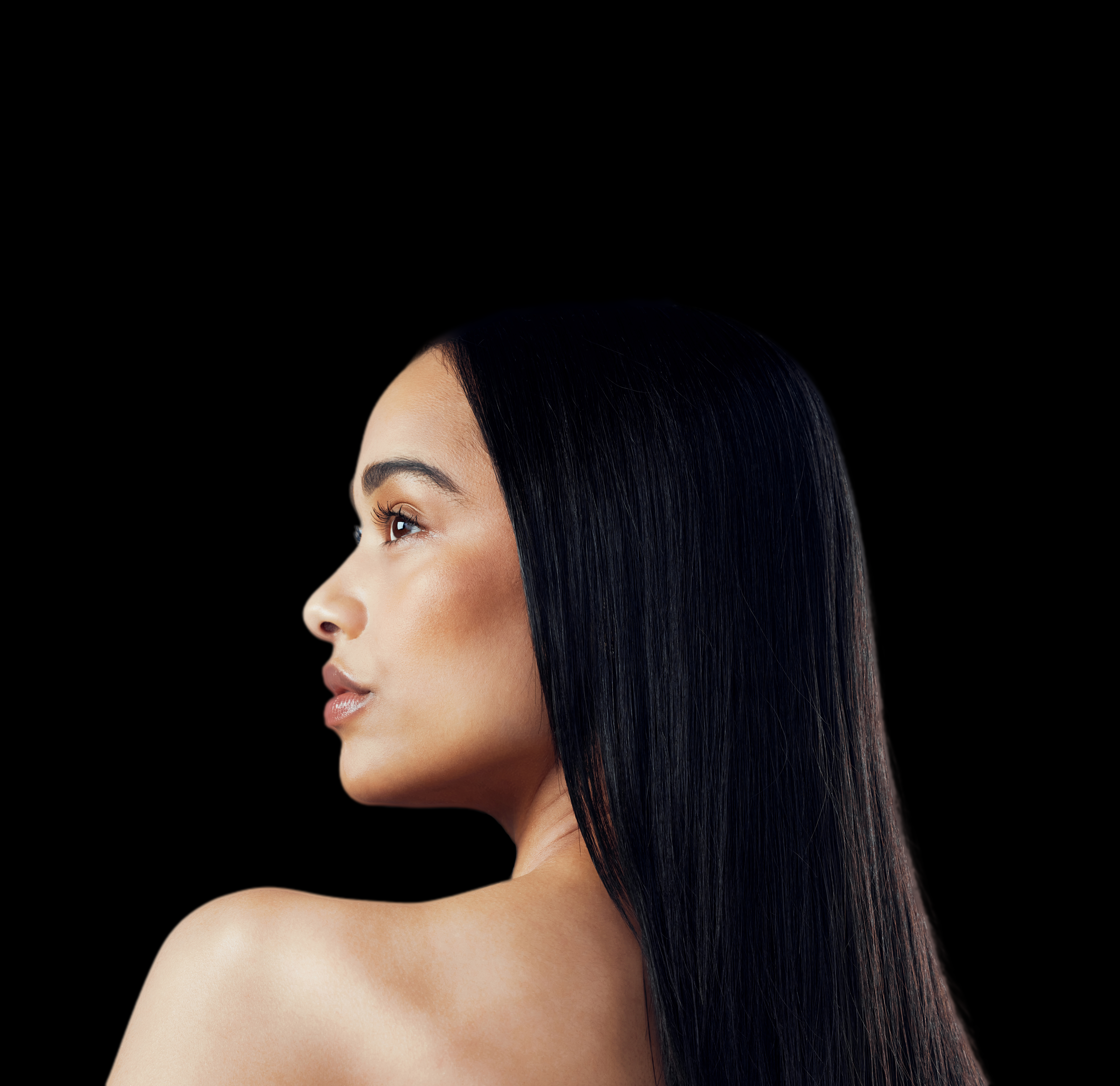 Profil kobiety z długimi, czarnymi włosami na czarnym tle. Patrzy w lewo, z makijażem.