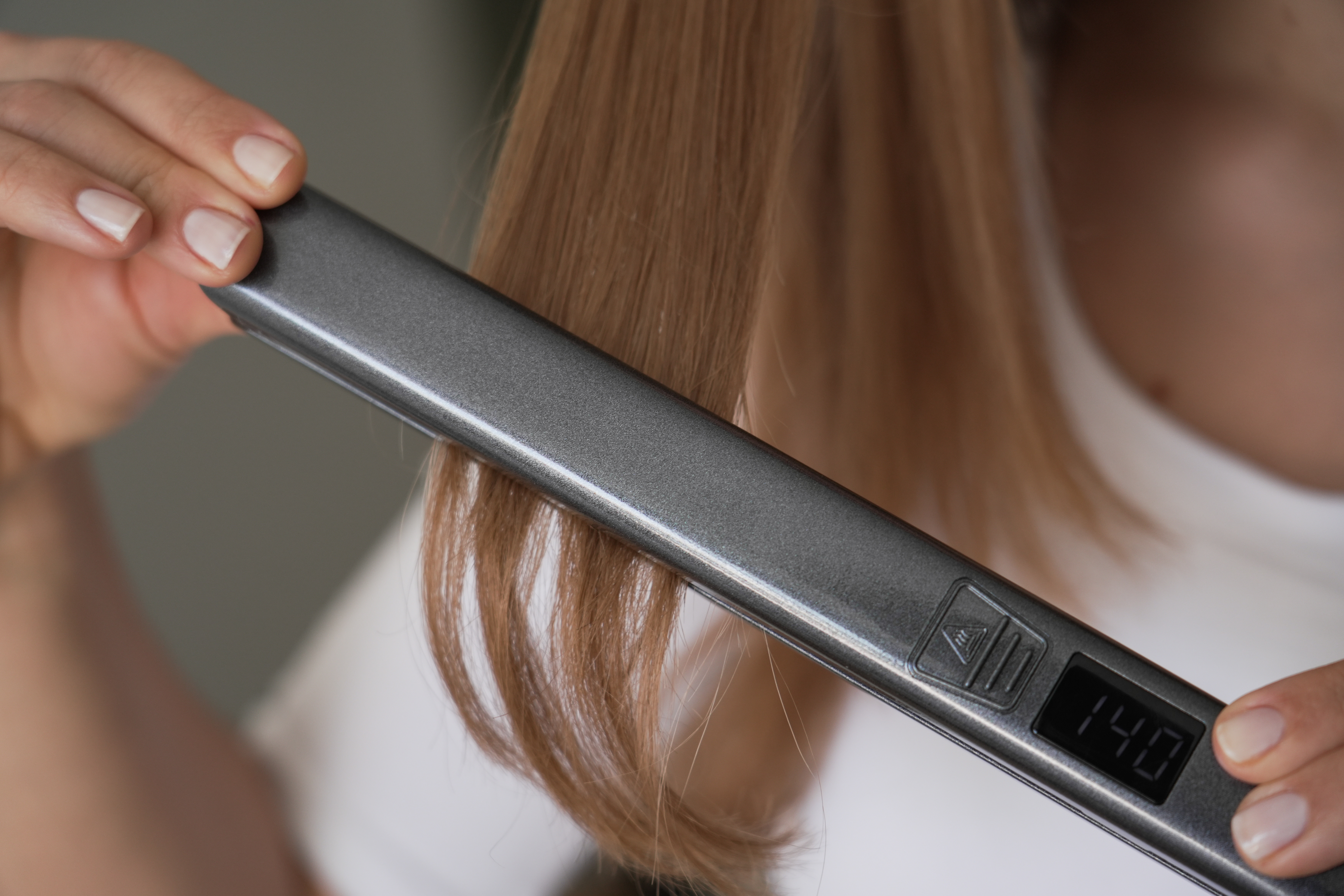Osoba używa prostownicy do jasnobrązowych włosów. Urządzenie pokazuje 140 stopni.