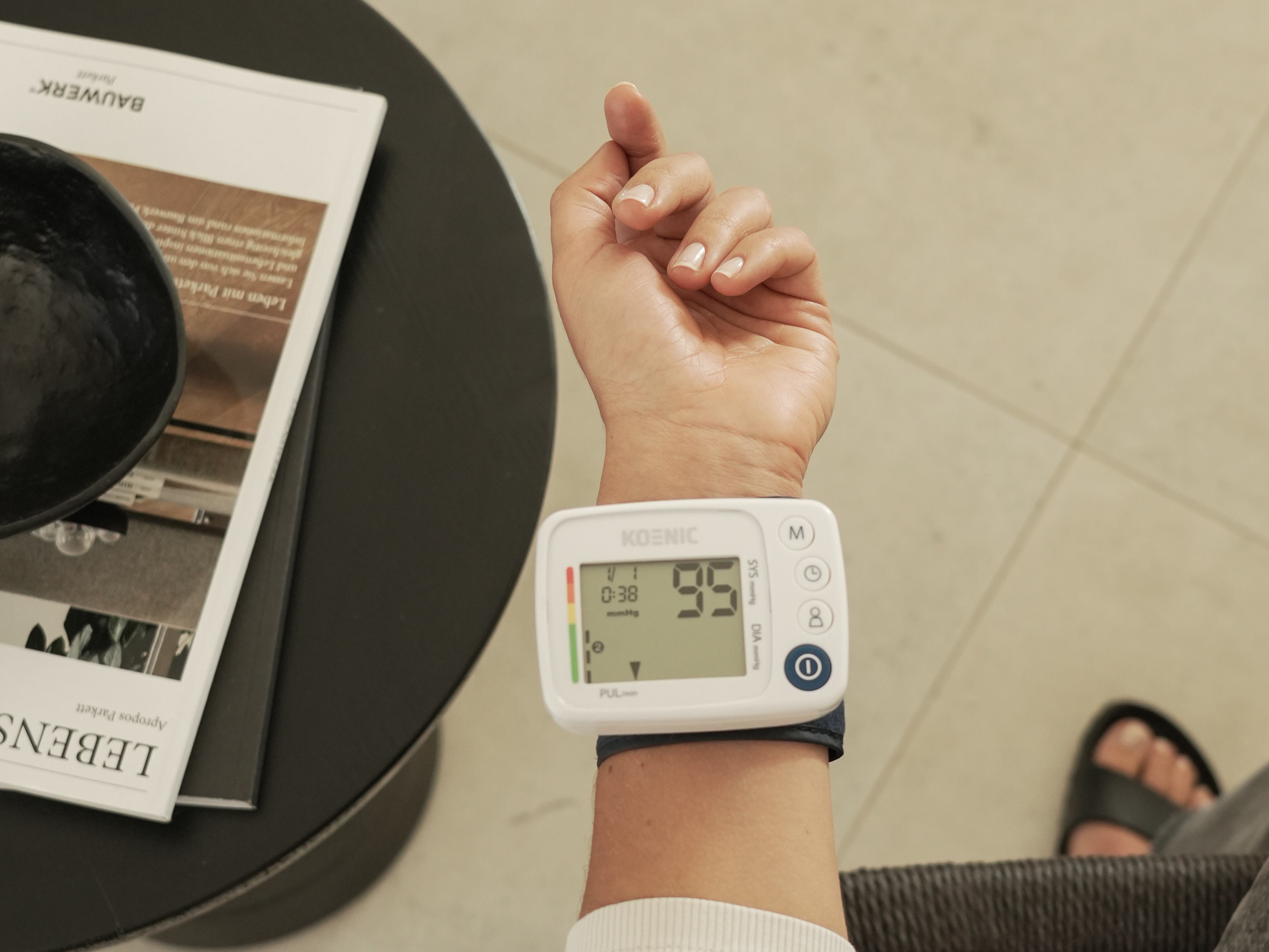 Nadgarstek z ciśnieniomierzem. Czasopismo i czarna miska na stole.