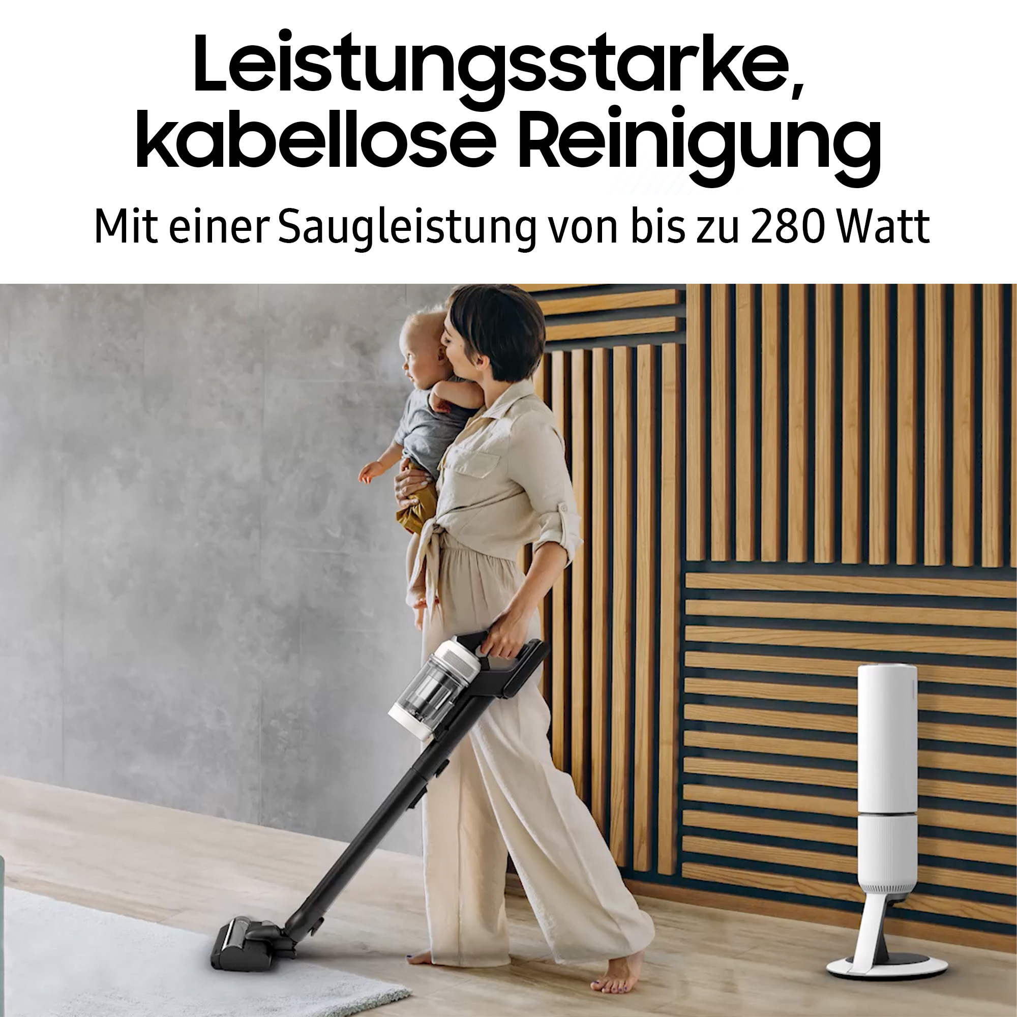 Frau mit Baby, benutzt einen schwarzen, kabellosen Staubsauger. Hintergrund: Holzpaneelwand und weiße Reinigungsstation.