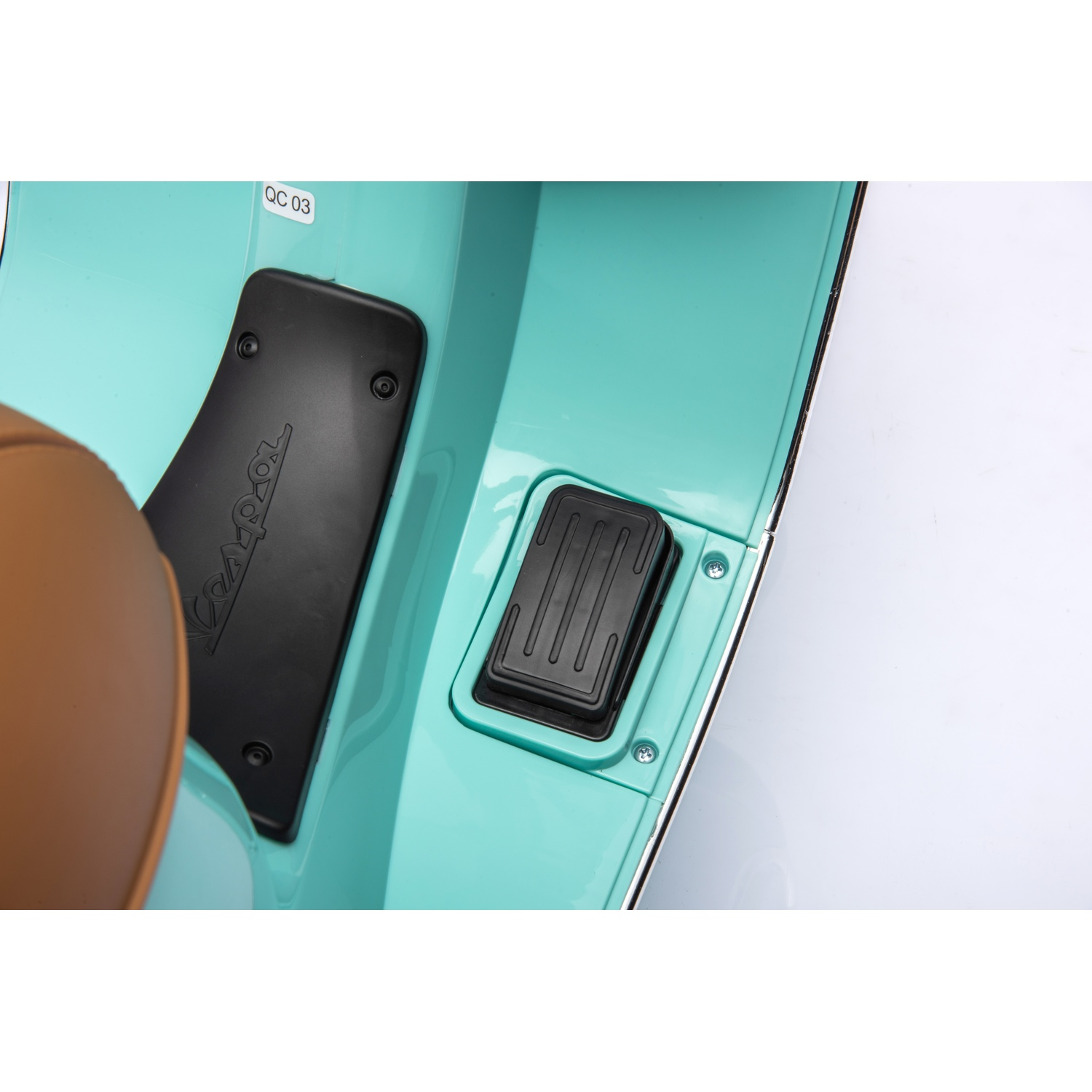 Gros plan sur le repose-pieds d'un scooter turquoise. Il y a une pédale noire, un siège marron et un autocollant indiquant QC 03.