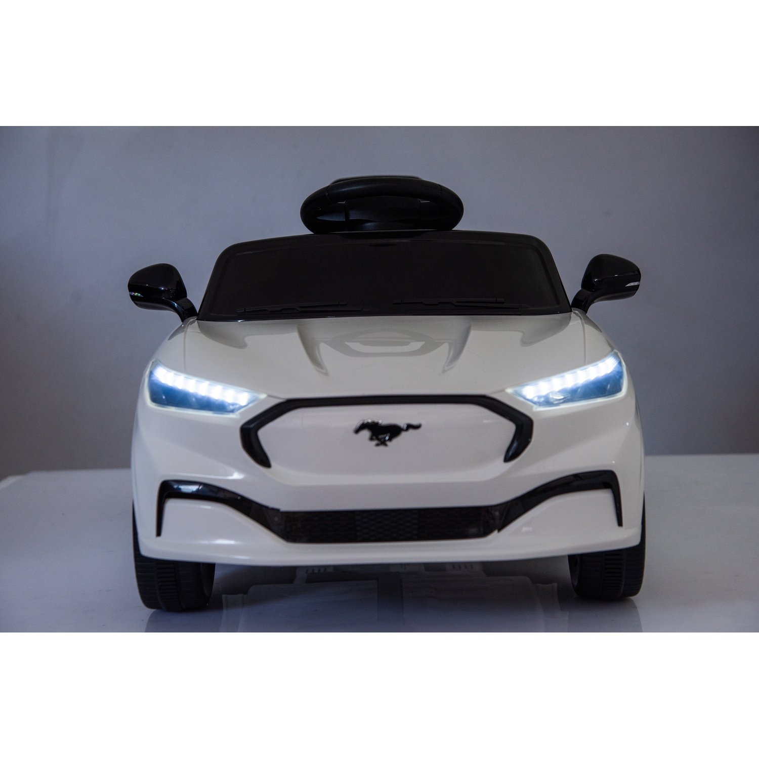 Une voiture jouet blanche avec un toit noir et des détails noirs. La voiture a des phares et un logo mustang.