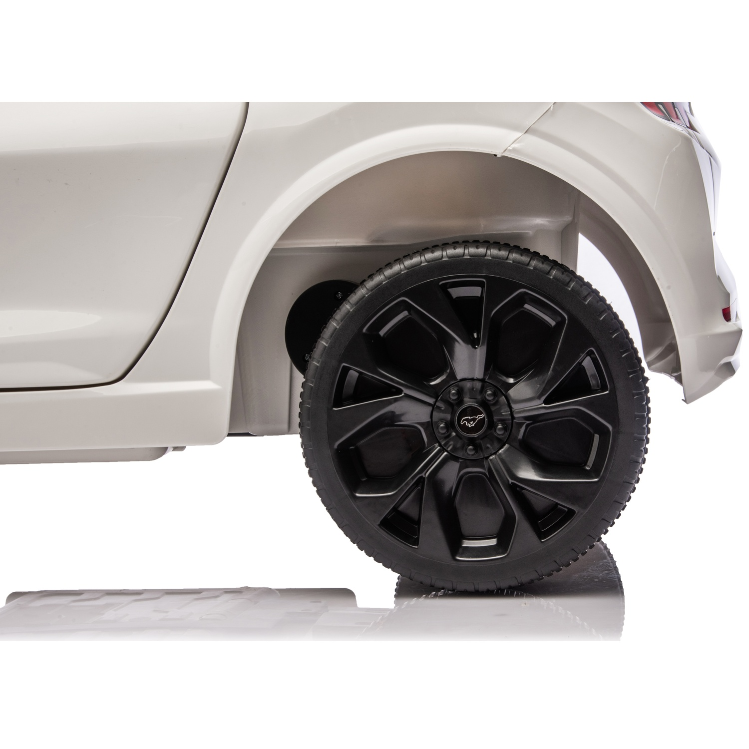 Le côté d'une voiture jouet blanche est visible, avec une roue noire. La voiture est sur une surface blanche, reflétant la roue.