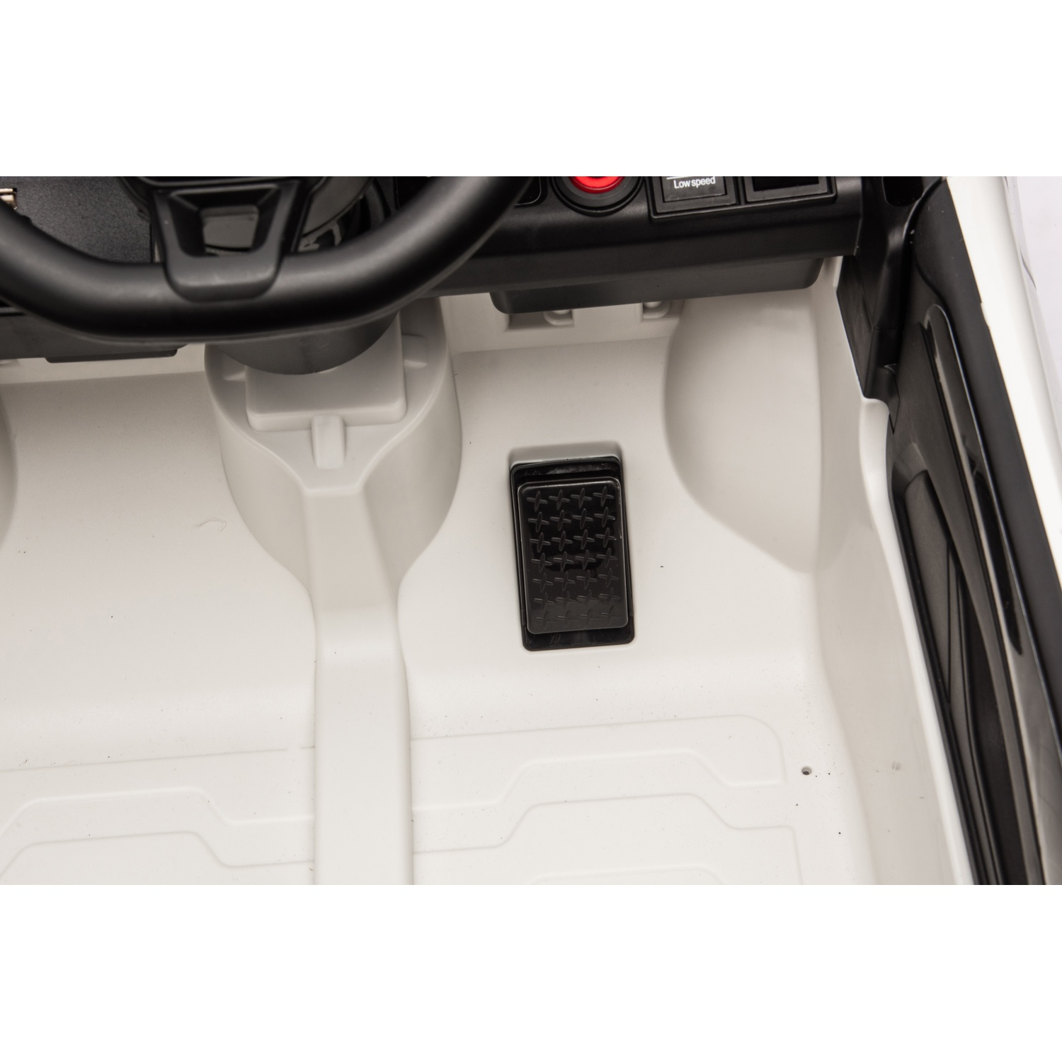 Intérieur d'une voiture jouet : volant, tableau de bord et pédale. Intérieur blanc avec détails noirs.