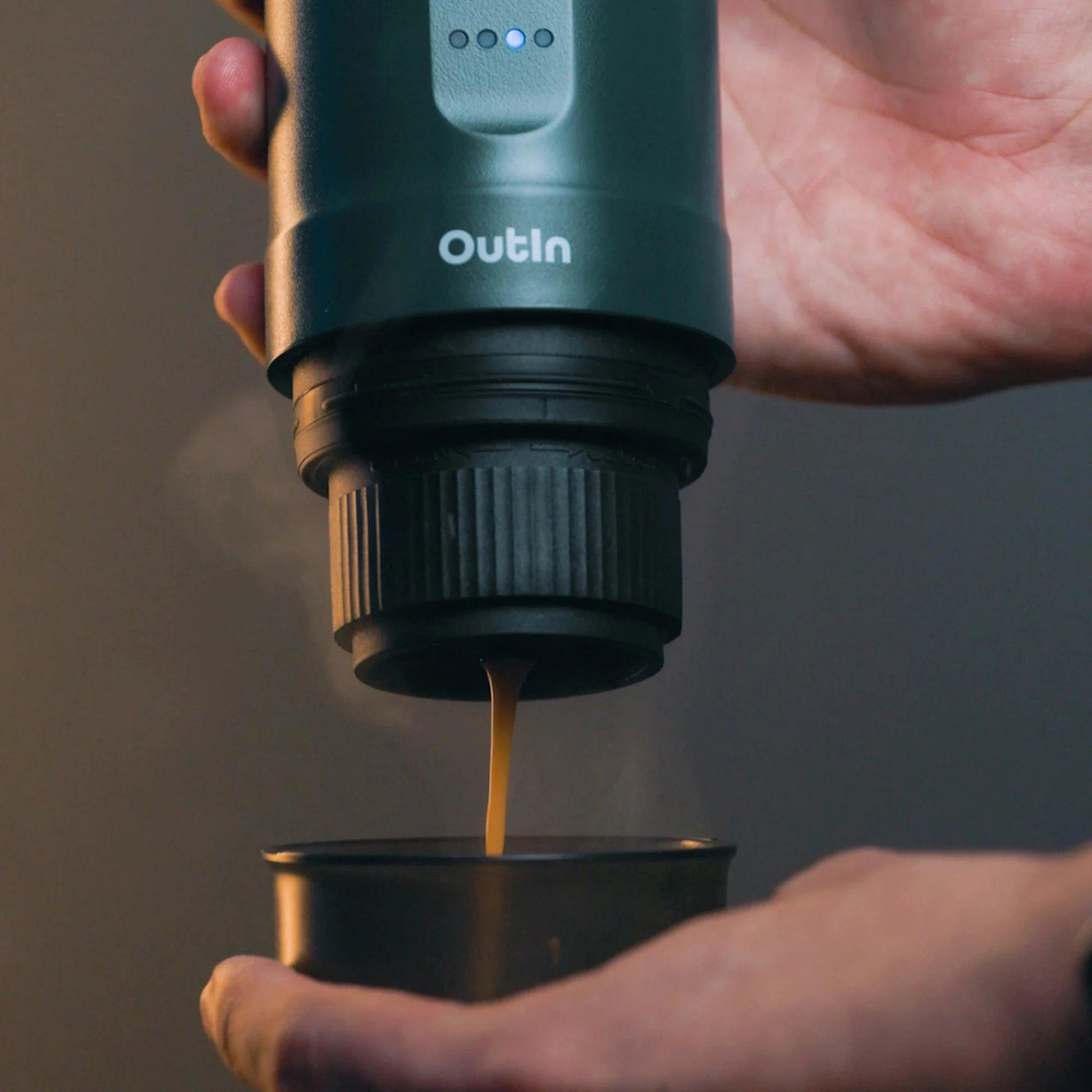 Eine Person gießt Kaffee aus einem tragbaren Kaffeezubereiter in eine Tasse. Der Maker ist dunkelgrün.