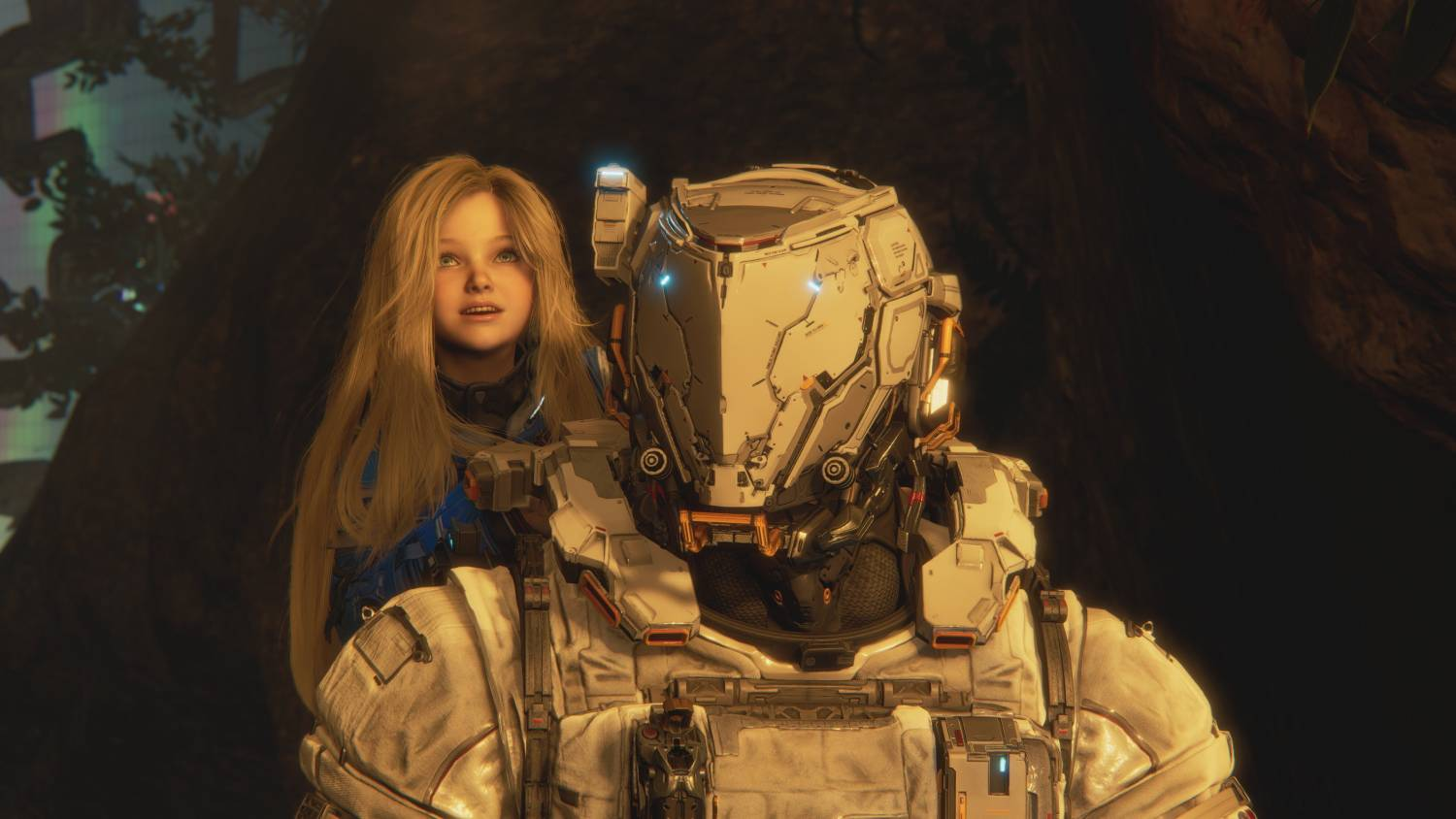 Una chica rubia mira hacia arriba, detrás de una figura futurista blindada en un entorno similar a una cueva.