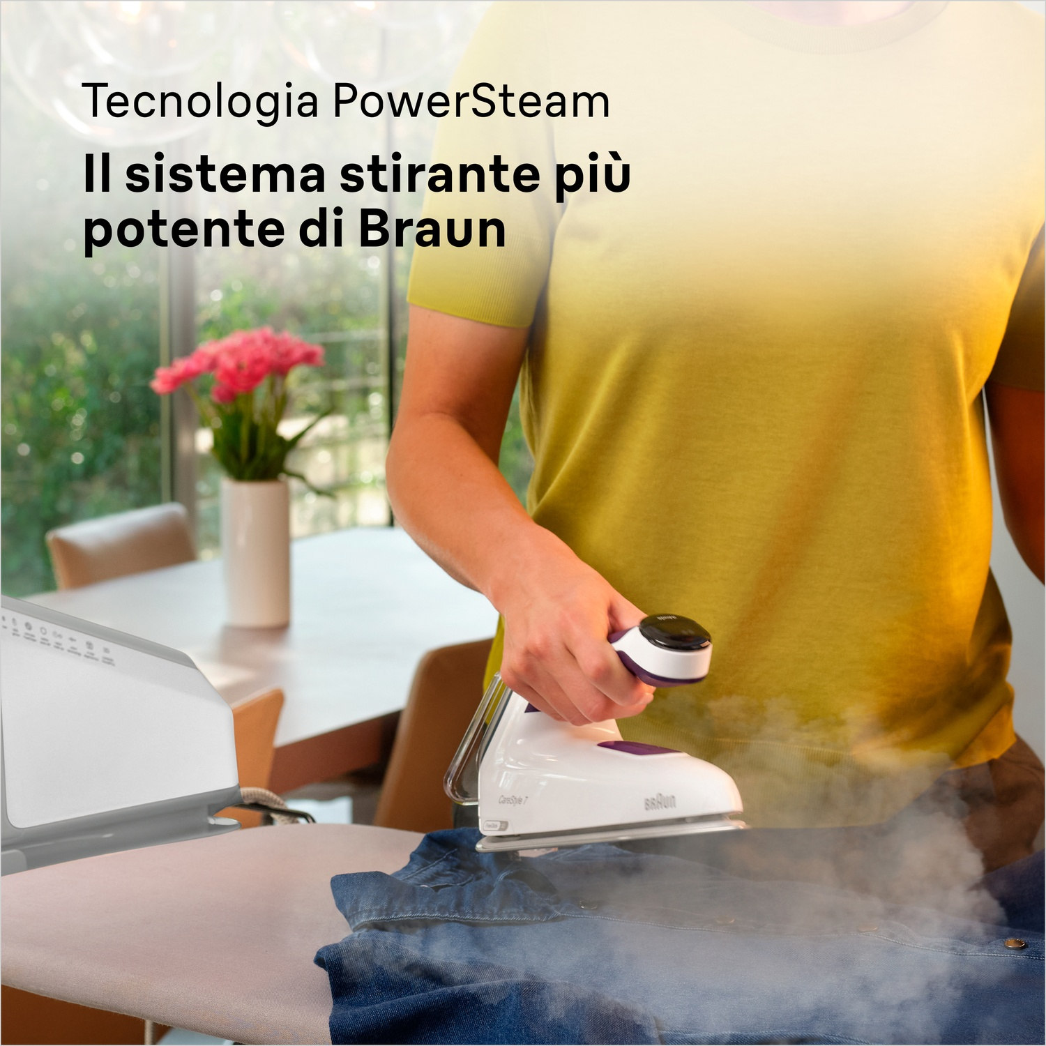 Una persona stira una giacca di jeans blu con un ferro da stiro bianco e viola. Il vapore sale. Il logo Braun è visibile.