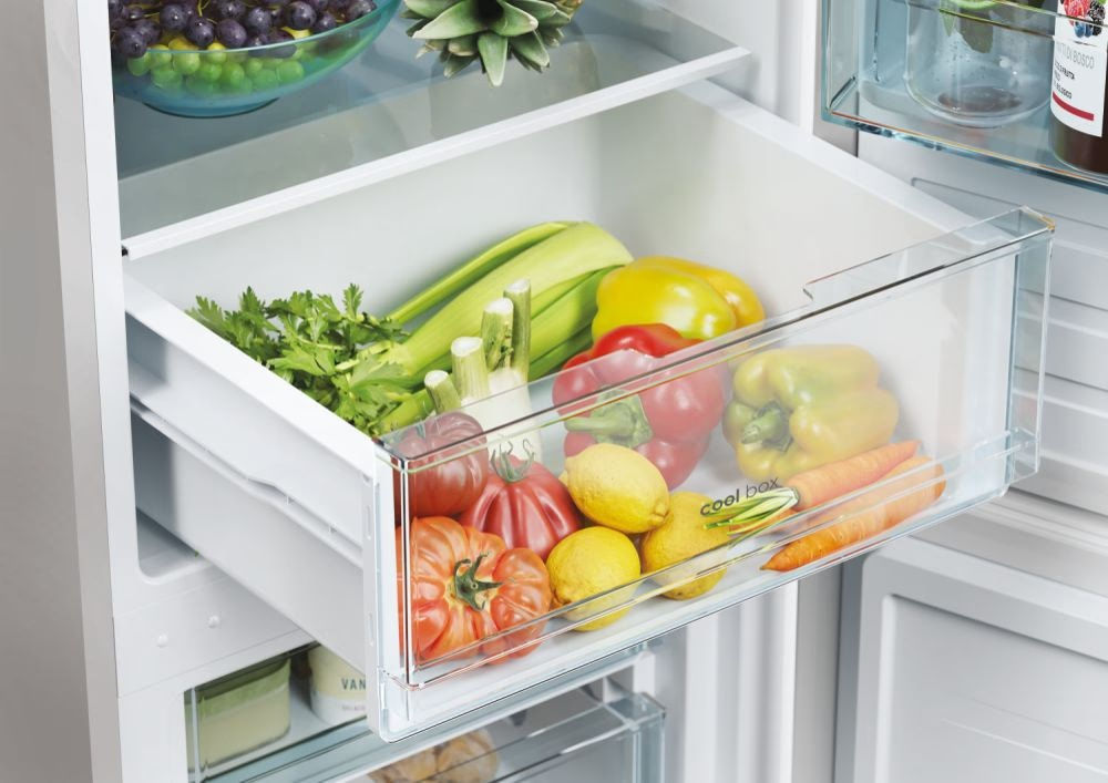 Refrigerador con cajón lleno de verduras: tomates, limones, pimientos, apio y zanahorias.