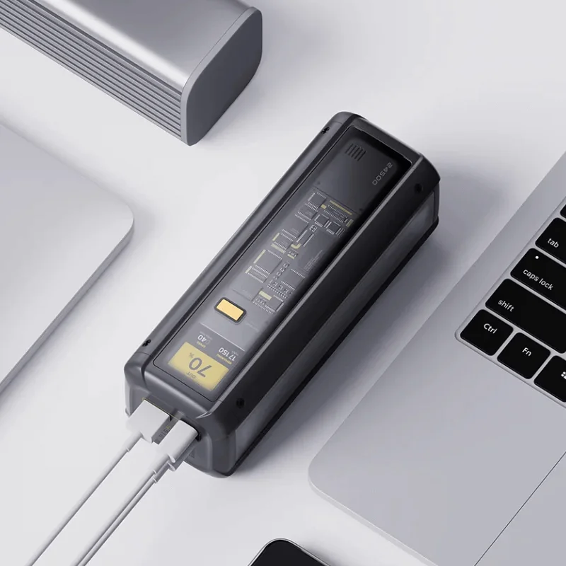 Un banco de energía negro con dos cables blancos conectados, rodeado por un portátil, una tableta y un dispositivo plateado. La pantalla muestra el 70% de carga.