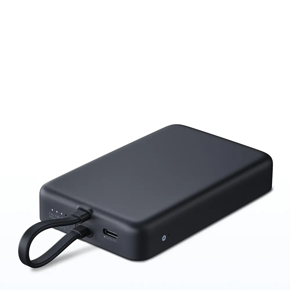 Un power bank negro con una correa está sobre una superficie blanca. Los cables están enchufados. El power bank tiene un puerto USB-C.