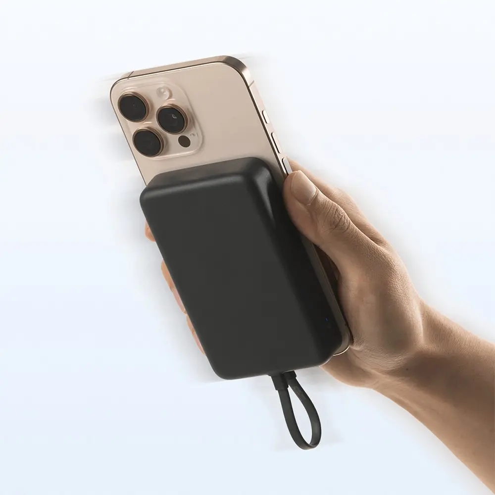 Una mano sostiene un iPhone dorado con un banco de energía negro adjunto. El fondo es blanco. El banco de energía tiene un lazo negro.