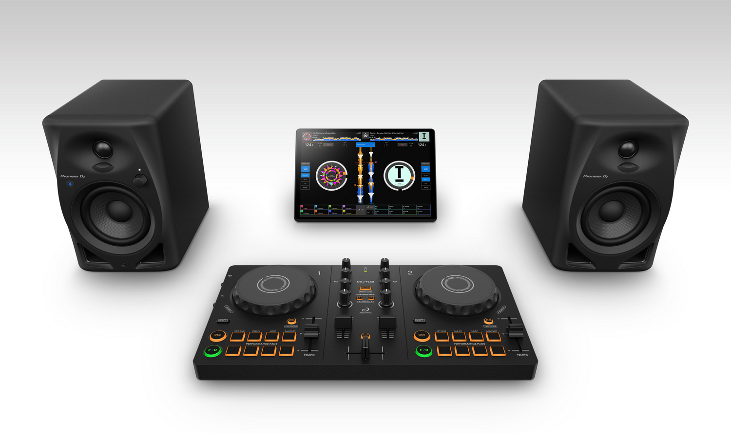 Equipo de DJ con altavoces negros, una mesa de mezclas y una tableta que muestra software de música sobre superficie blanca.