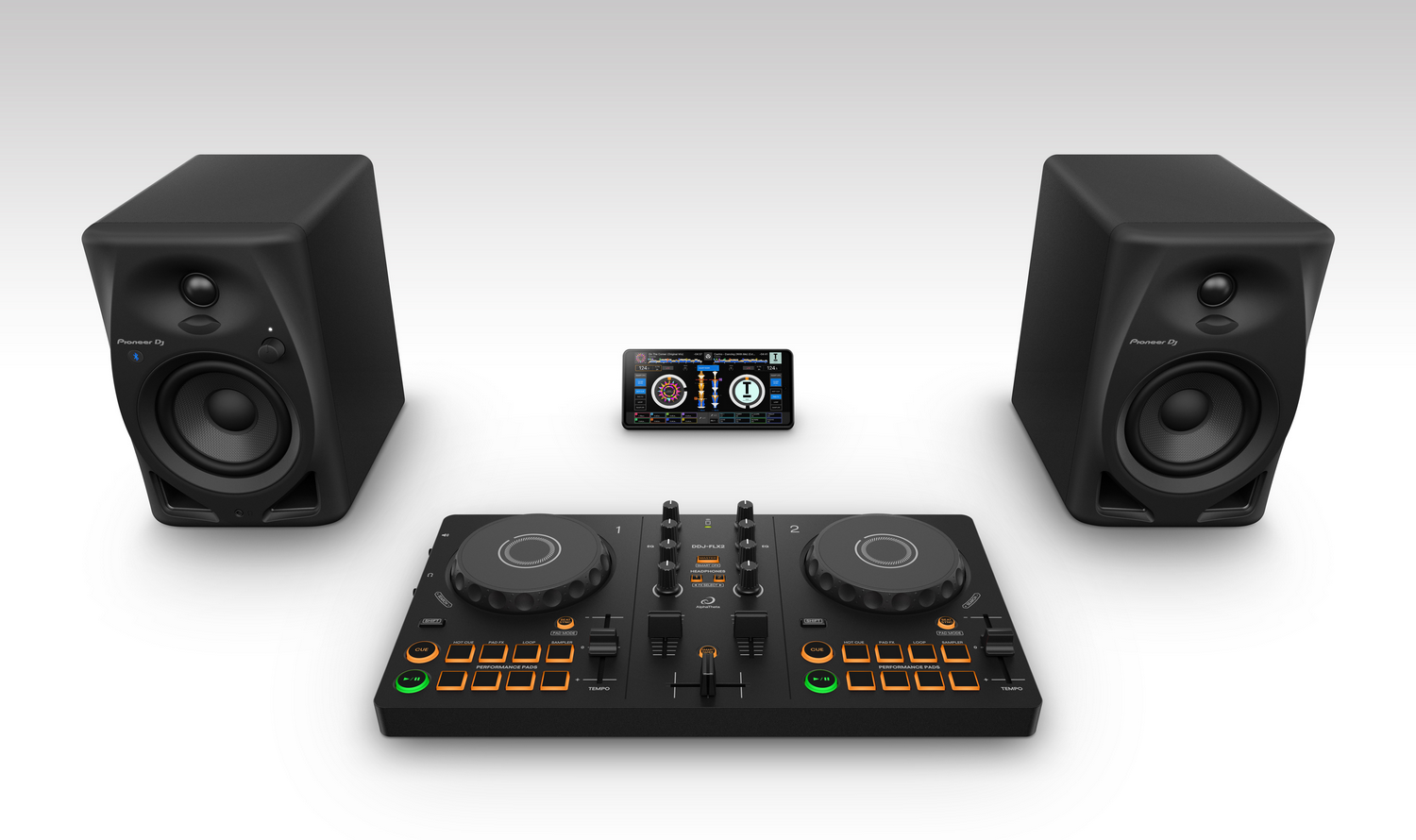 Equipo de DJ con altavoces negros, un controlador de DJ y un smartphone que muestra la interfaz de música, todo sobre una superficie blanca.