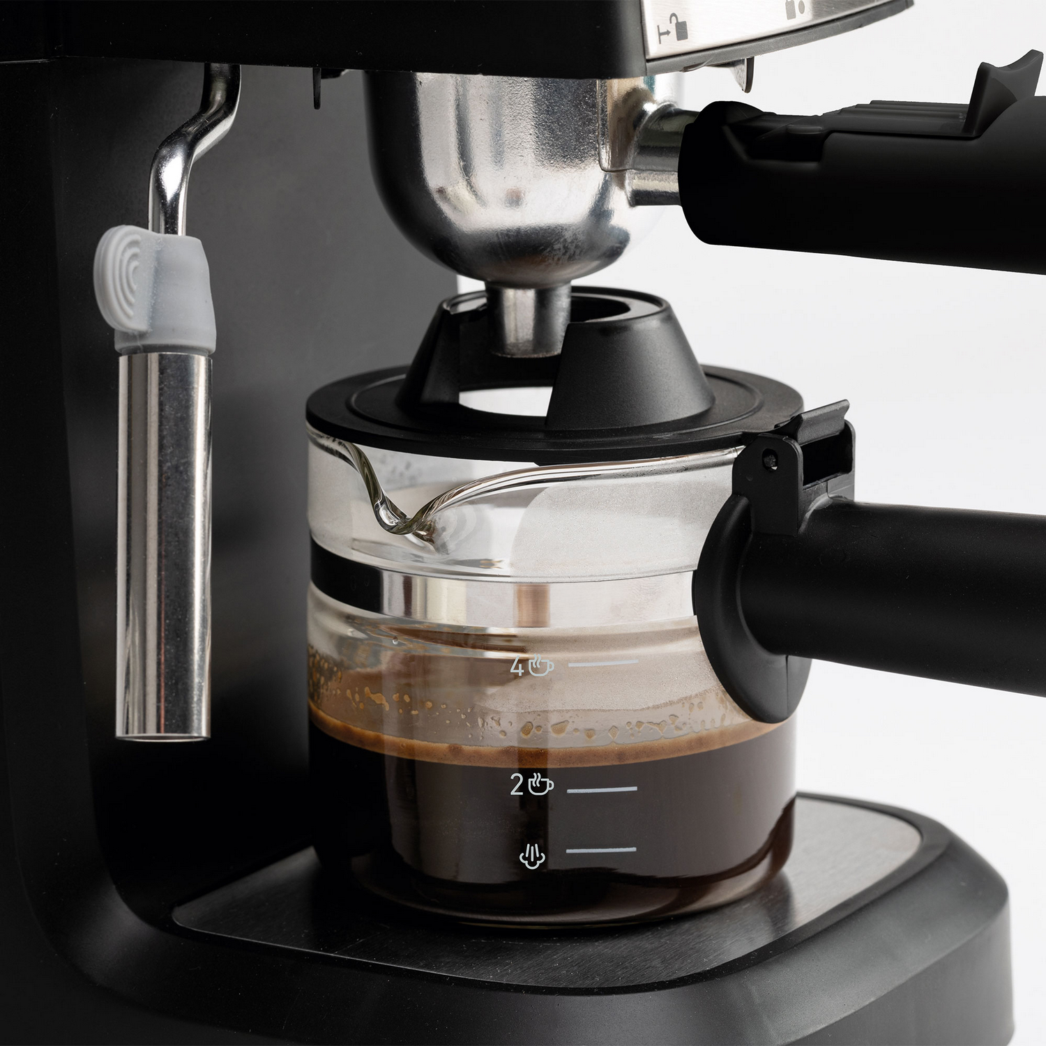 Primer plano de una máquina de espresso. Una jarra de vidrio contiene café oscuro. La máquina tiene componentes negros y plateados.