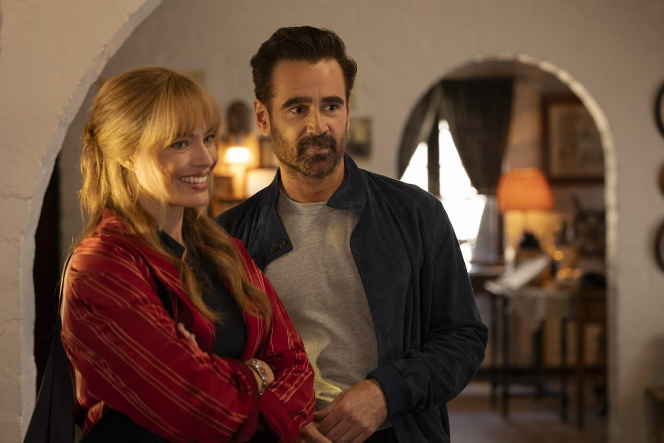 Ein Mann und eine Frau lächeln in einem Innenraum. Die Frau trägt Rot und der Mann eine blaue Jacke. Der Hintergrund zeigt einen Bogen und eine Lampe.