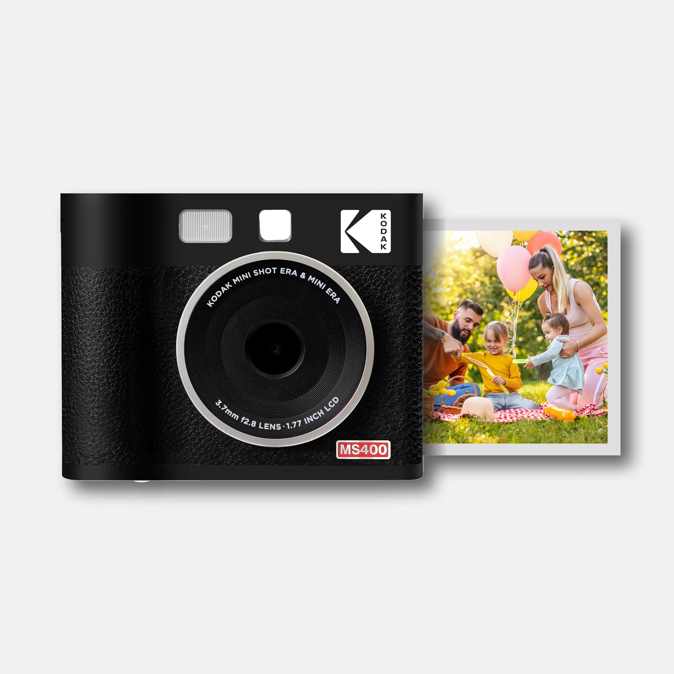 Siyah Kodak fotoğraf makinesi ve aile pikniği fotoğrafı. Makinede Kodak logosu var. Aile parkta, balonlarla.