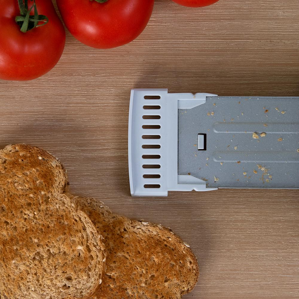Dos rebanadas de tostadas, tomates y una bandeja de migas de tostadora sobre una superficie de madera.