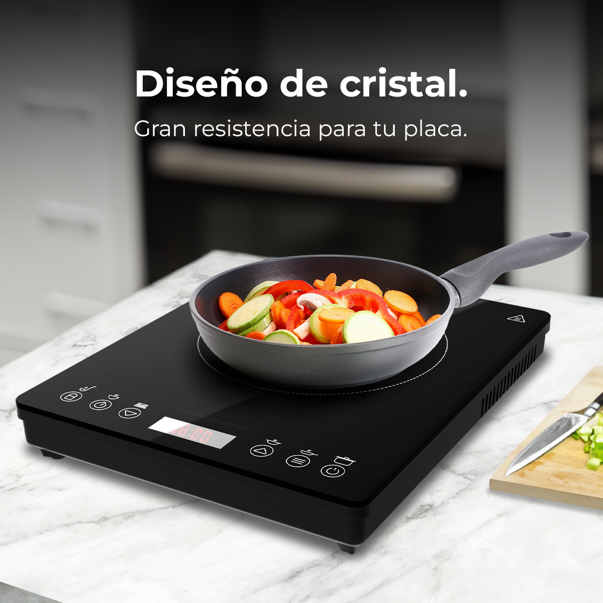 Una placa de inducción negra con una sartén de verduras sobre una encimera de mármol. Un cuchillo y una tabla de cortar están al fondo.