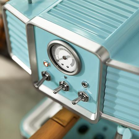 Primer plano de una máquina de espresso azul de estilo retro. Tiene un manómetro, interruptores y un asa de madera. Hay detalles plateados.