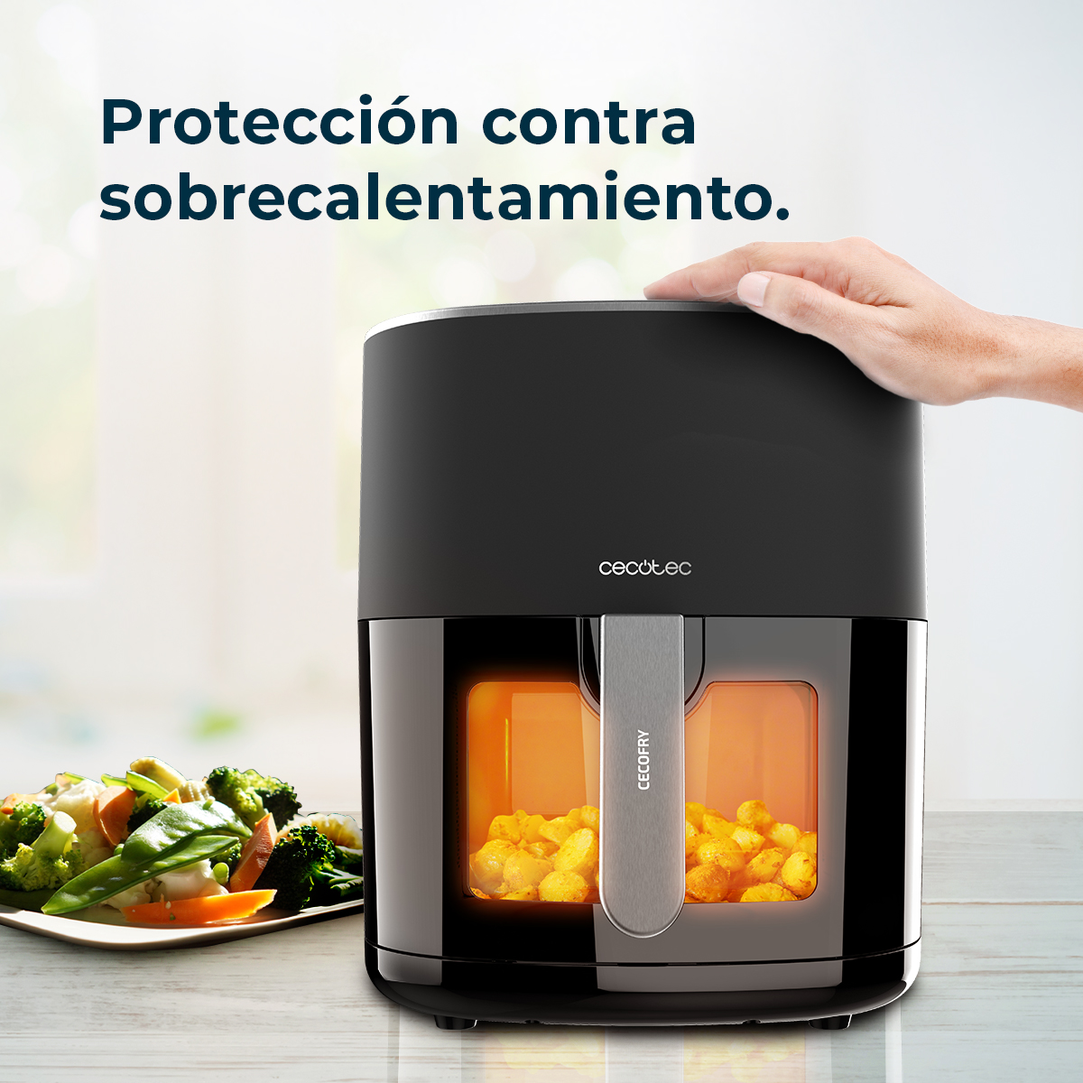 Freidora de aire negra con asa, mano en la parte superior. Verduras en plato. Texto: Protección contra sobrecalentamiento.