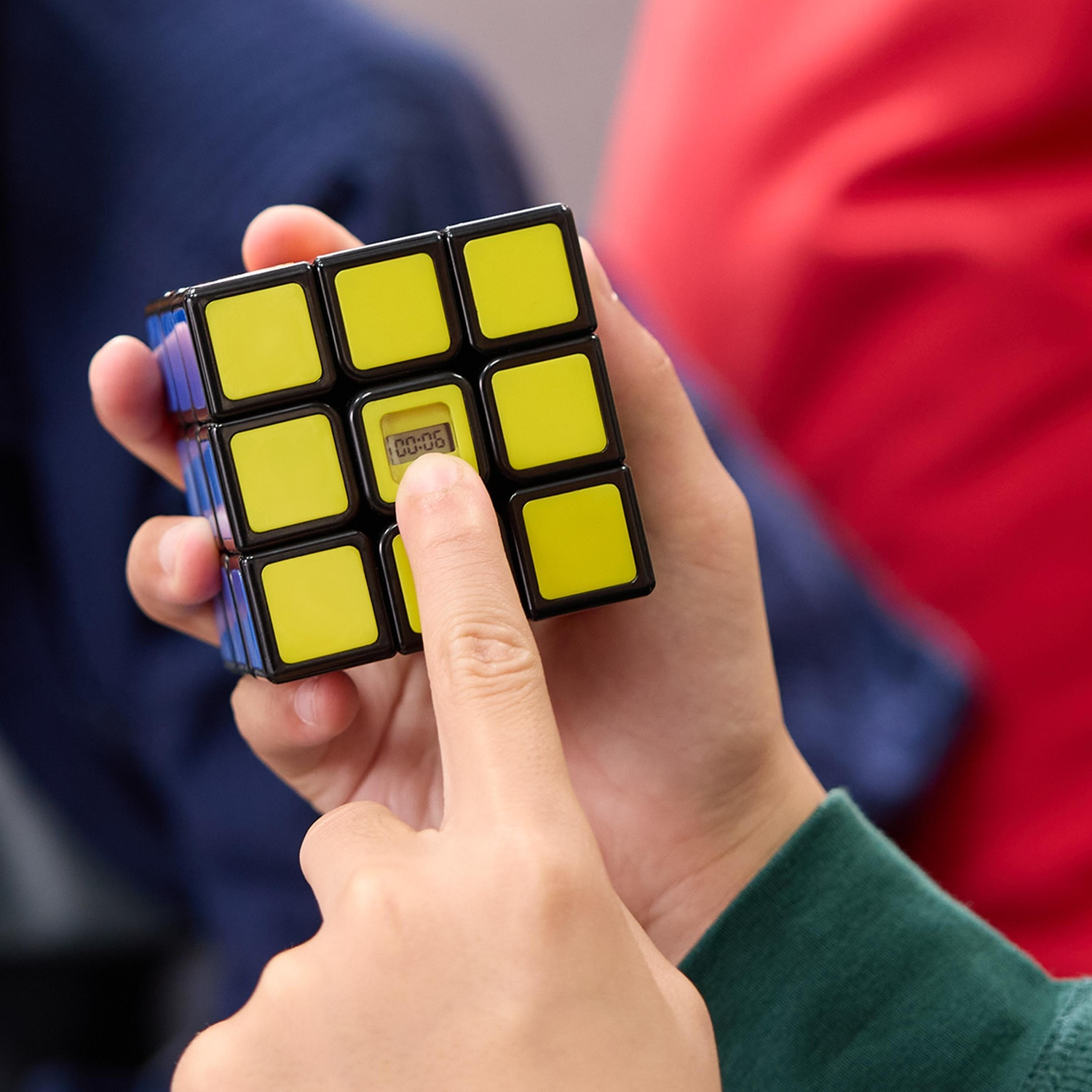 Una persona tiene in mano un cubo di Rubik con quadrati gialli e neri, il timer indica 00:06. Sfondi blu e rossi visibili.