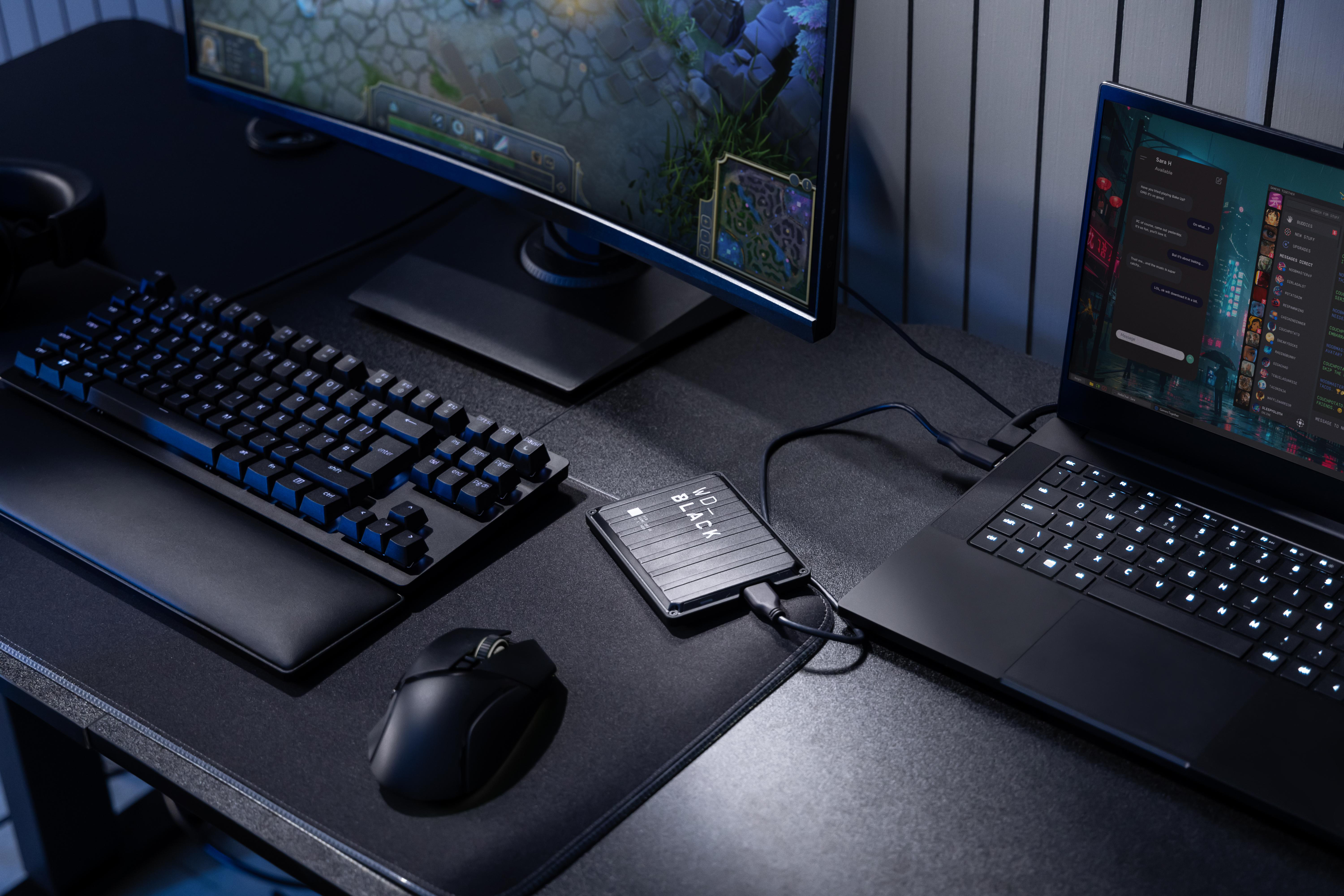 Gaming-Setup mit Tastatur, Maus, Monitor, Laptop und externer Festplatte. Alles in Schwarz, Szene mit Blautönen beleuchtet.