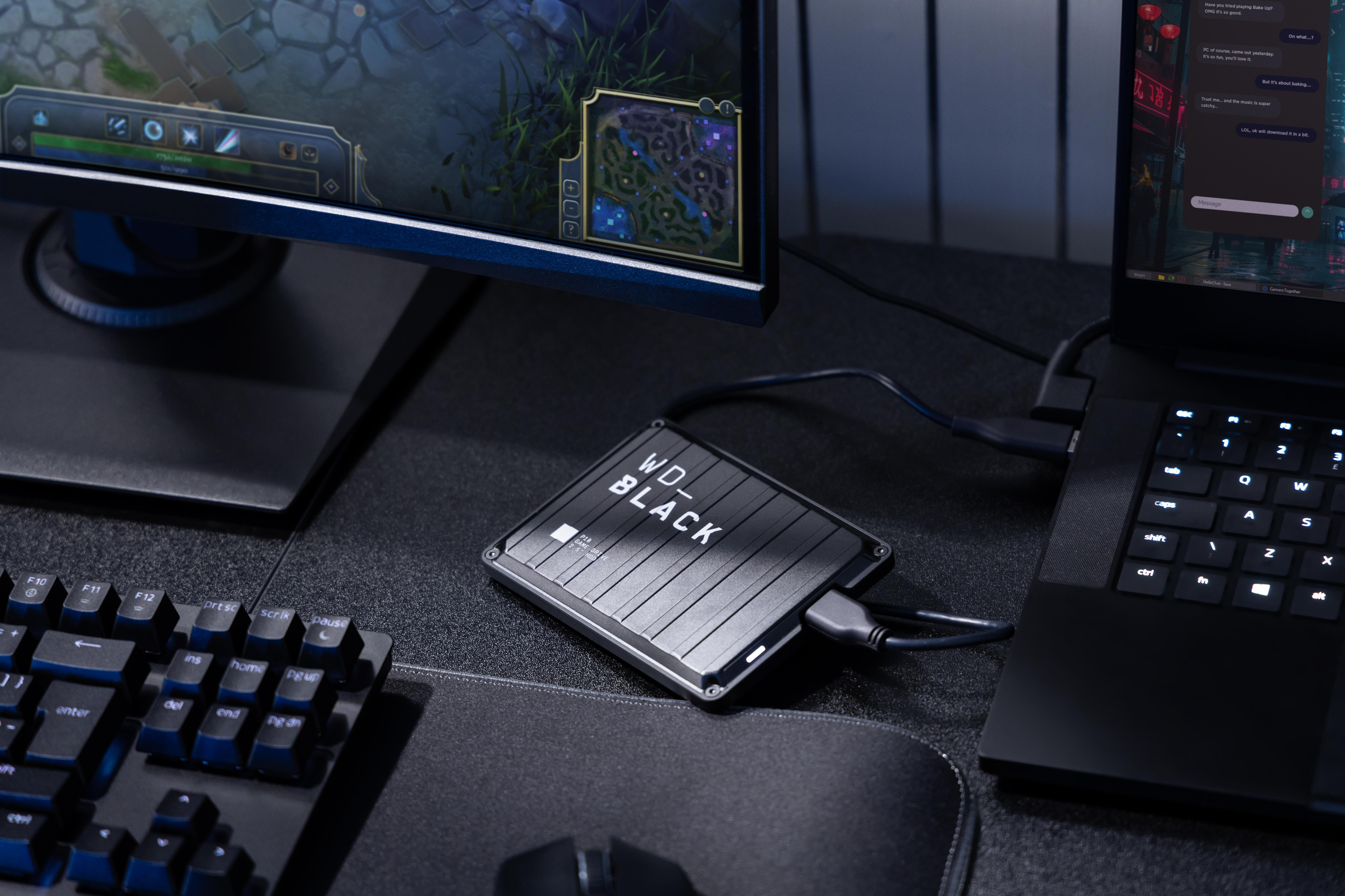 Ein Schreibtisch mit Monitor, Laptop, Tastatur und externer WD_BLACK Festplatte.