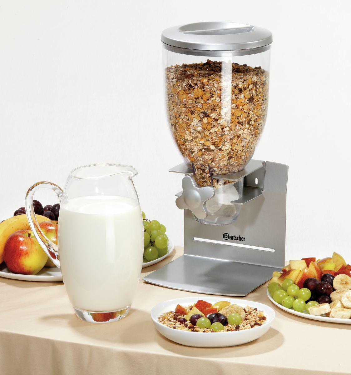 Ein Müslispender mit Obst und Milch. Ein klares Glas mit Müsli, ein Glas Milch und Obstteller auf einem Tisch.