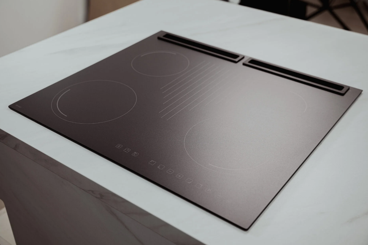 Czarna płyta indukcyjna na białym blacie. Ma cztery strefy gotowania i sterowanie dotykowe. Tło jest rozmyte.