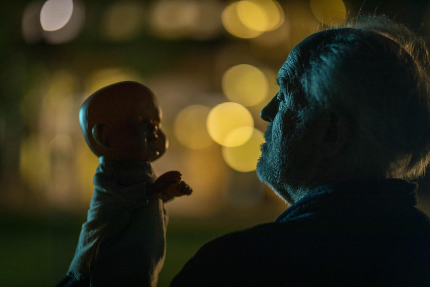 Ein Mann betrachtet eine Puppe. Die Puppe ist im Fokus, der Mann ist vor einem verschwommenen Hintergrund mit Bokeh-Lichtern silhouettiert.