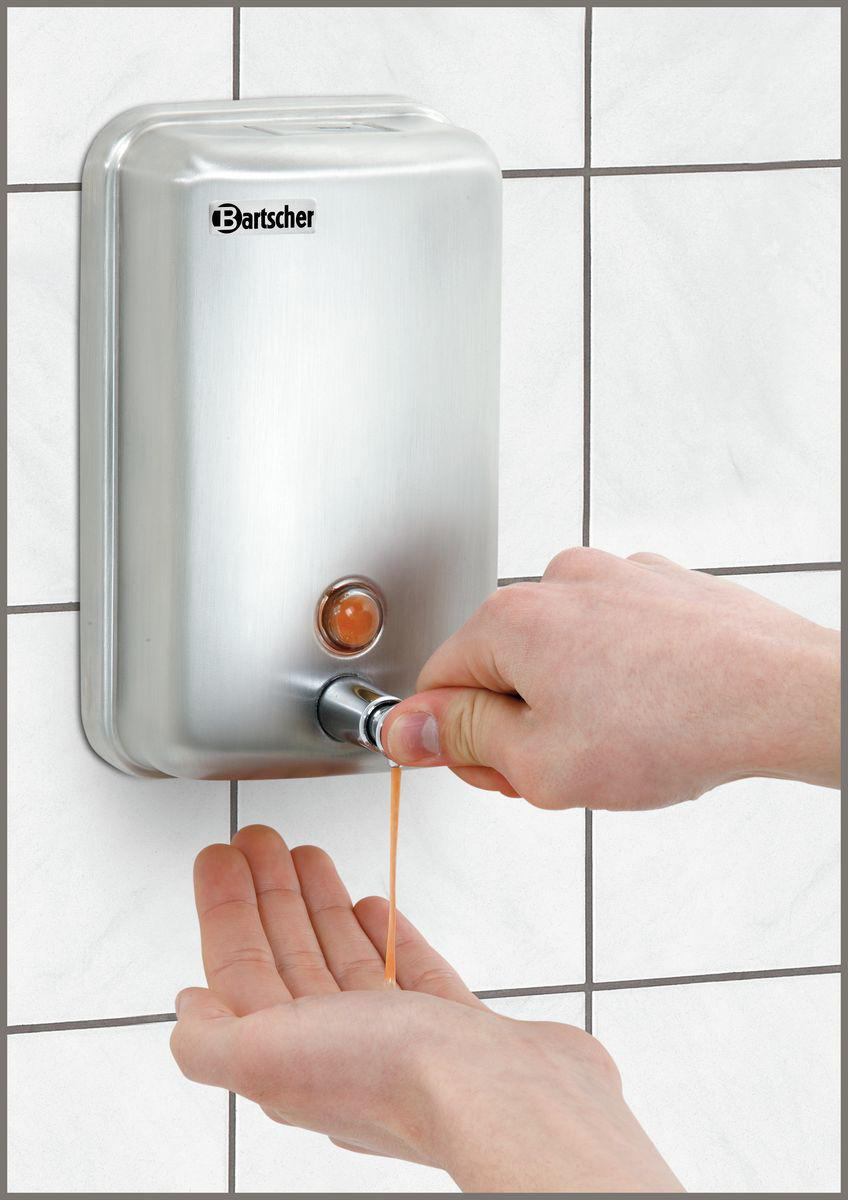 Eine Person gibt Flüssigseife aus einem Wandspender ab. Der Spender ist aus Edelstahl. Die Seife ist orange.