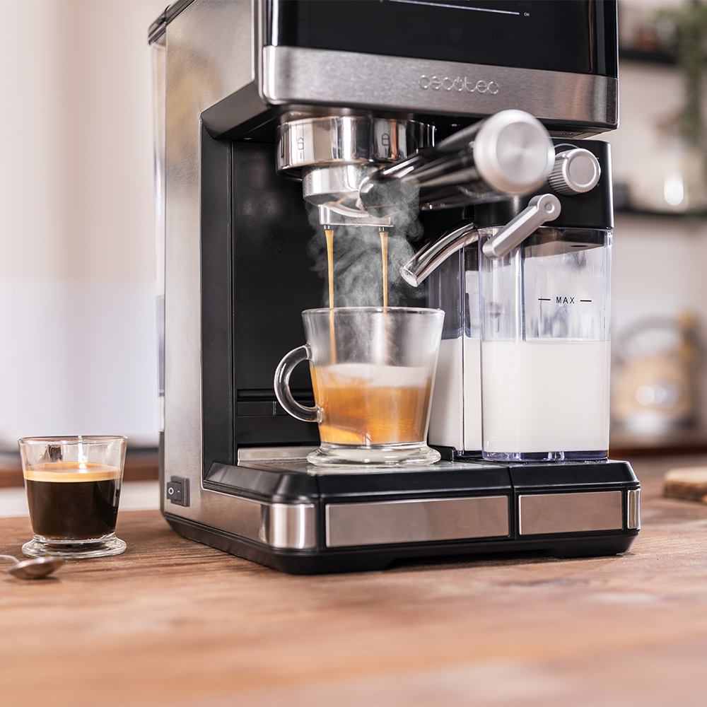Máquina de espresso preparando café. Una taza de vidrio se llena de café. Un vaso pequeño de café está en la mesa de madera.