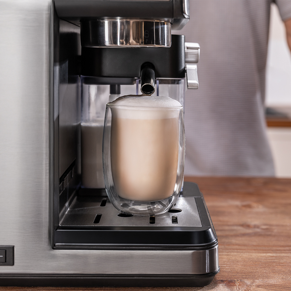 Máquina de espresso dispensando un latte en un vaso. Una persona está en el fondo.