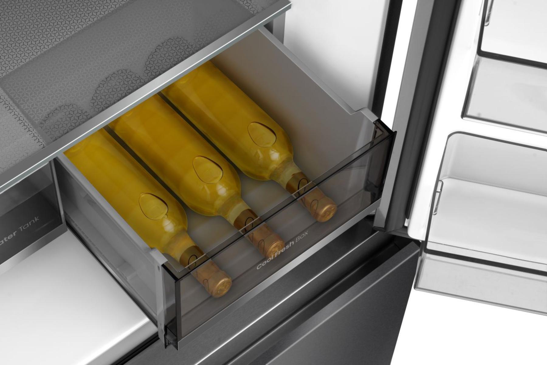 In einem Kühlschrank befinden sich drei Weinflaschen in einer Kühlbox. Die Flaschen haben gelbe Flüssigkeit mit braunen Korken. Der Kühlschrank ist geöffnet.