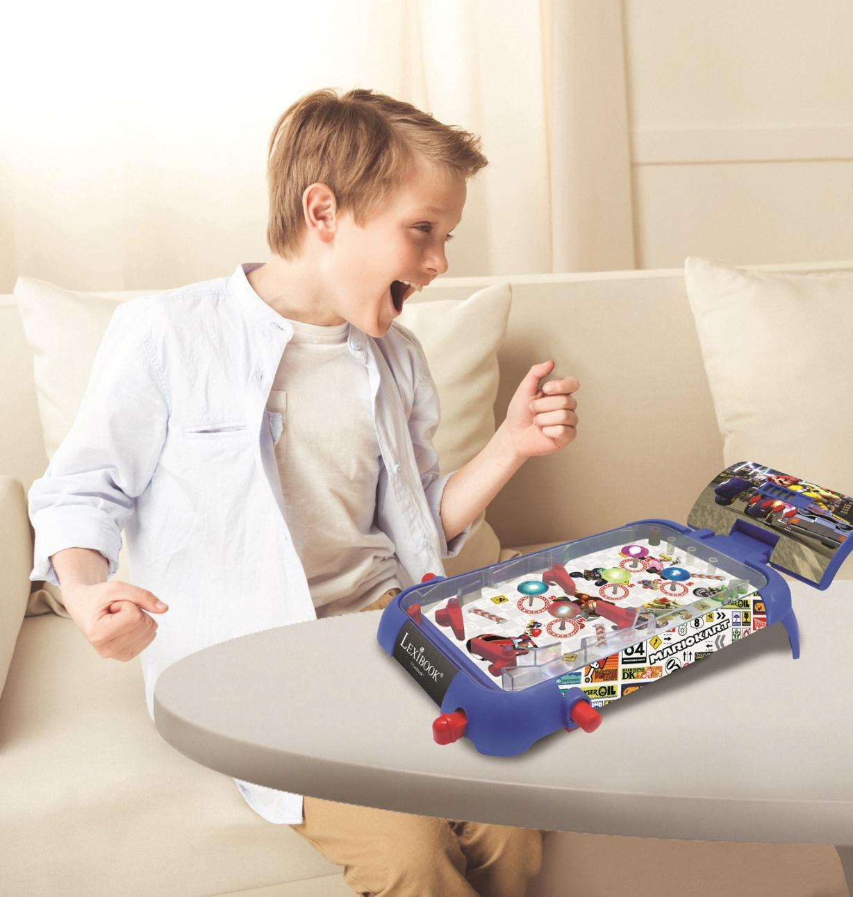 Ein Junge freut sich, während er ein Mario Kart Flipper Spiel spielt. Das blaue Spiel steht auf einem Tisch. Im Hintergrund ist eine Couch.