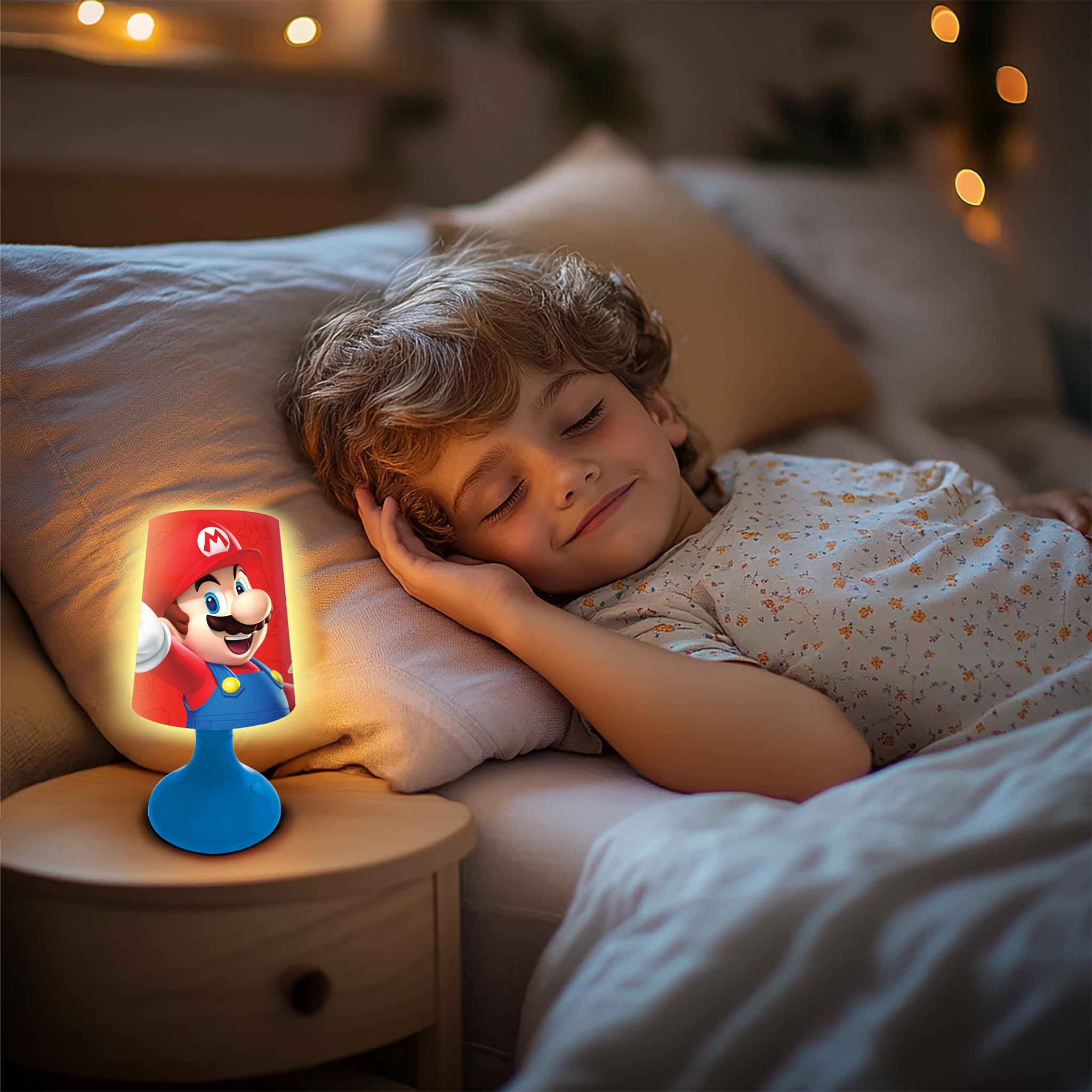 Ein Kind schläft neben einer Mario-Lampe auf einem Nachttisch. Der Raum ist schwach beleuchtet, mit weichem Bokeh.