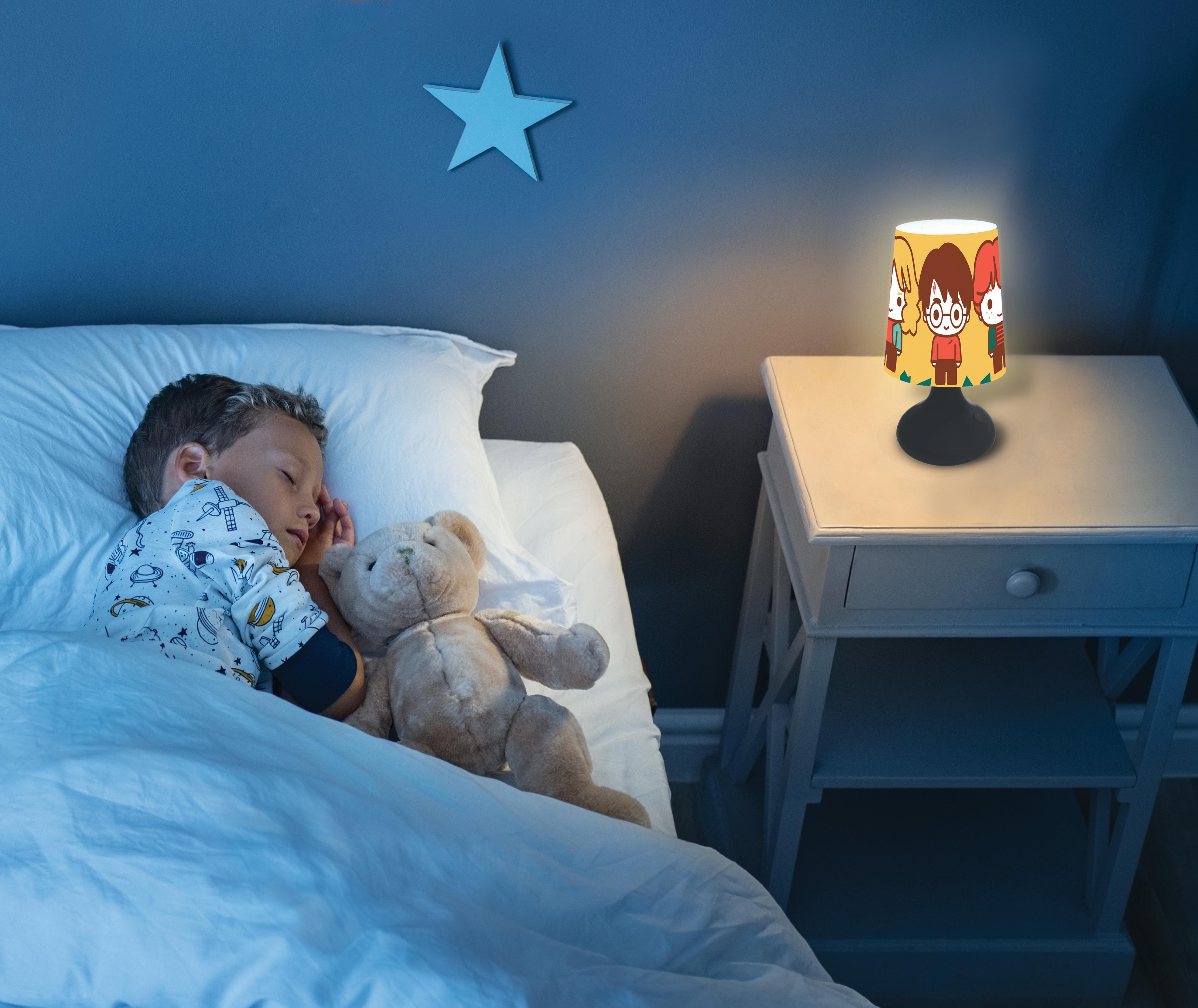 Ein schlafendes Kind mit Teddybär im Bett. Auf dem Nachttisch steht eine Lampe mit Zeichentrickfiguren.