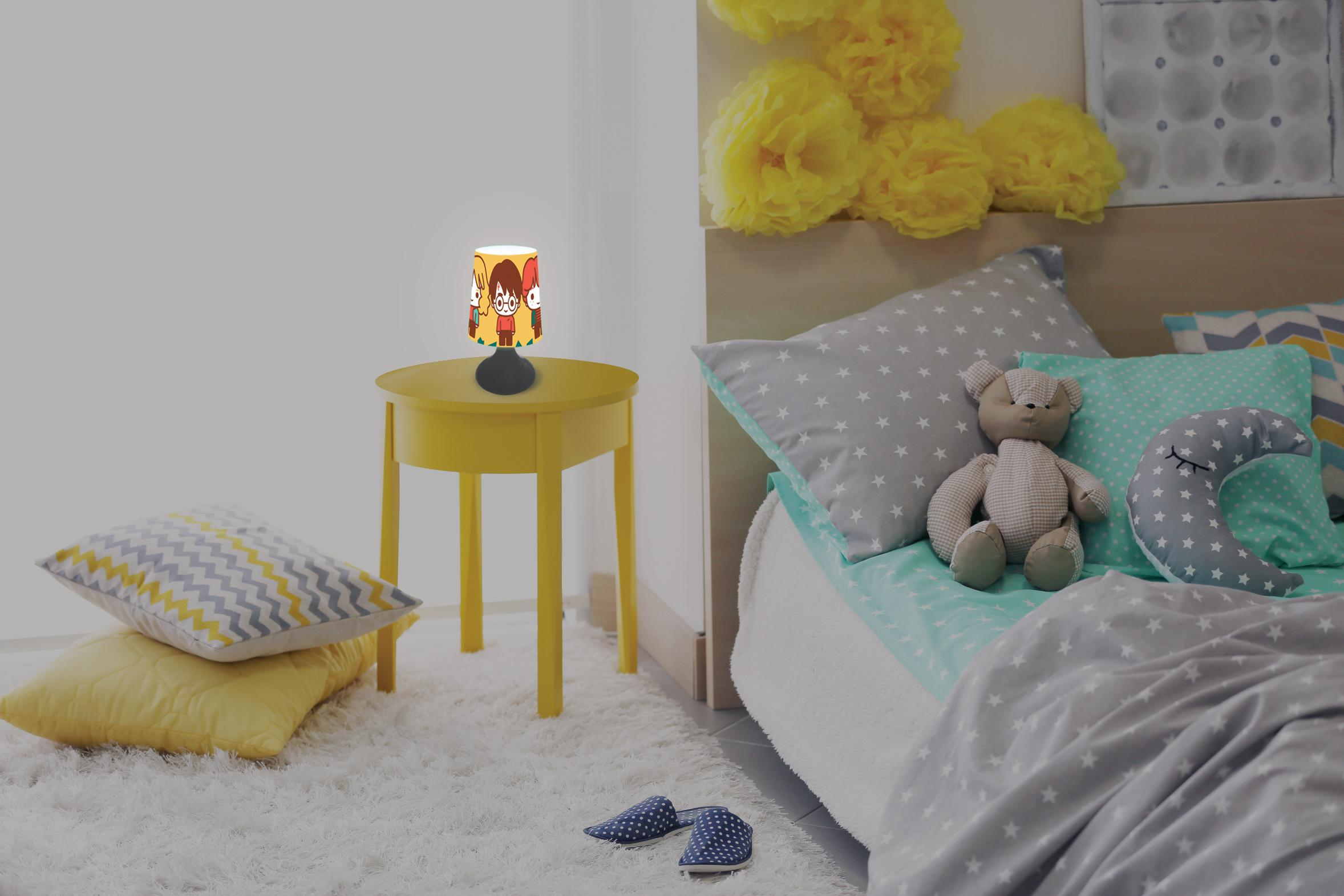 Schlafzimmerszene mit gelbem Tisch, Lampe, Kissen und Bett. Ein Teddybär und ein mondförmiges Kissen liegen auf dem Bett.