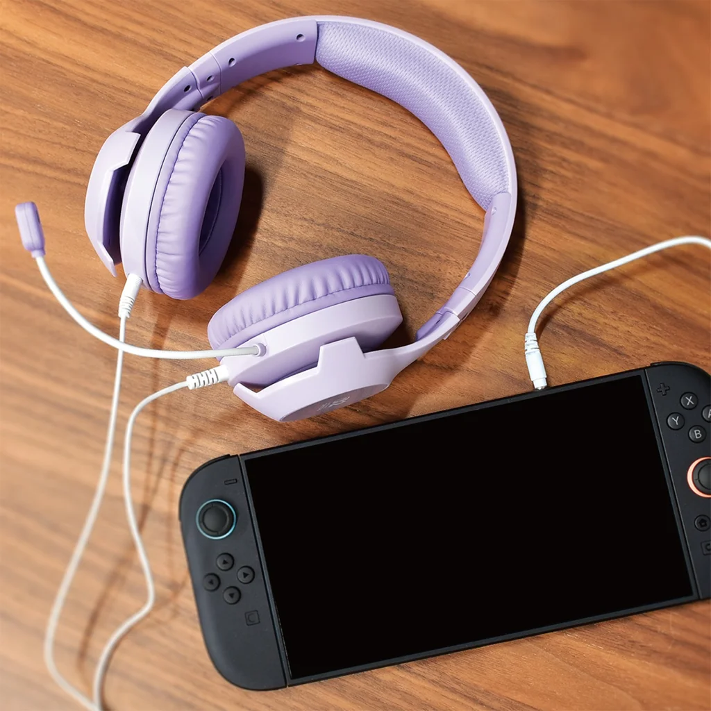 Ein lila Headset mit Mikrofon liegt auf einer Holzoberfläche neben einer schwarzen Spielkonsole.
