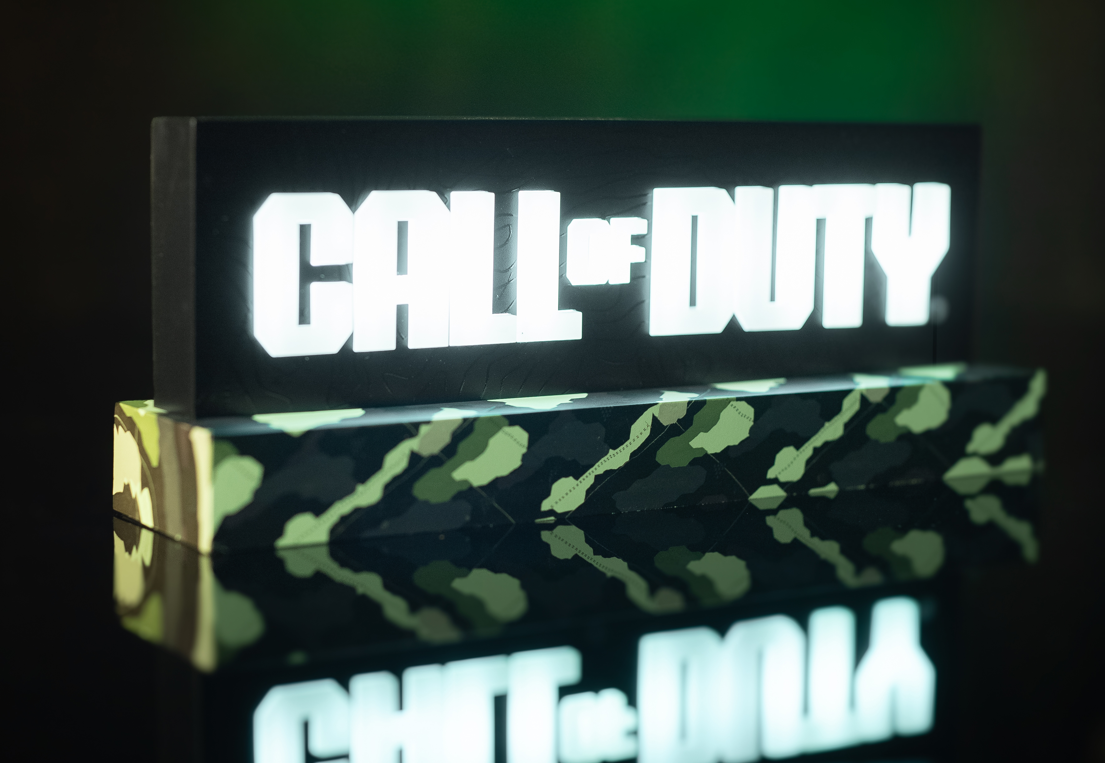 Call of Duty Schild. Weiße Buchstaben auf Schwarz. Camouflage-Basis. Das Schild ist beleuchtet.