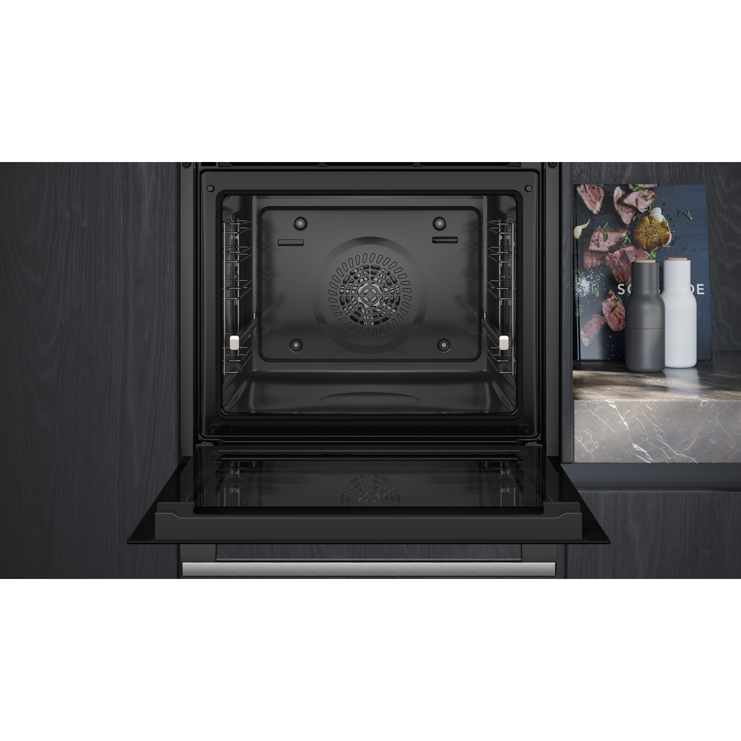 Open oven met interieur met roosters en ventilator. Kookboek en zout/pepermolens staan rechts op een aanrecht.