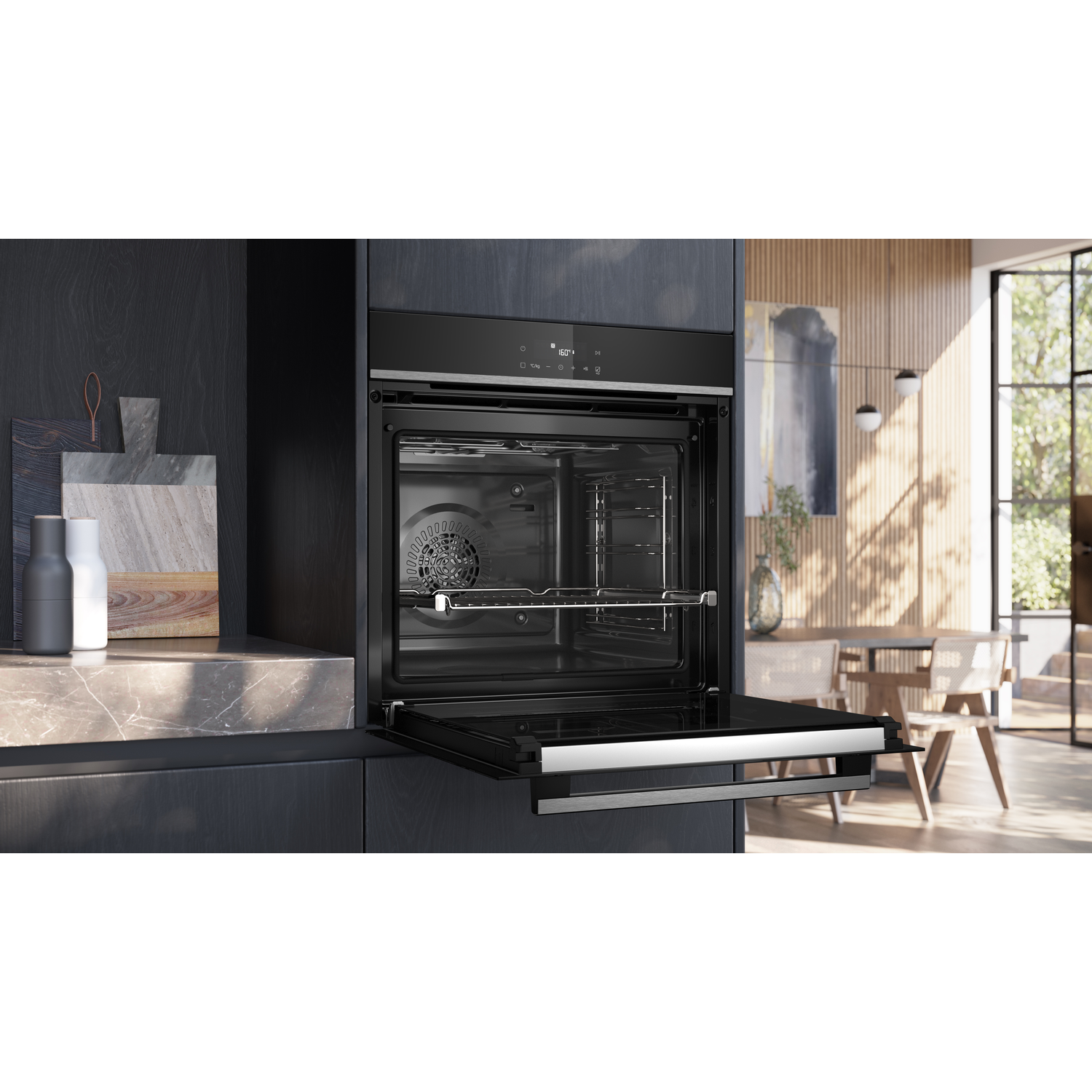 Open black oven in a dark kitchen, showing interior with rack. Marble countertop with bottles and cutting boards in the background.