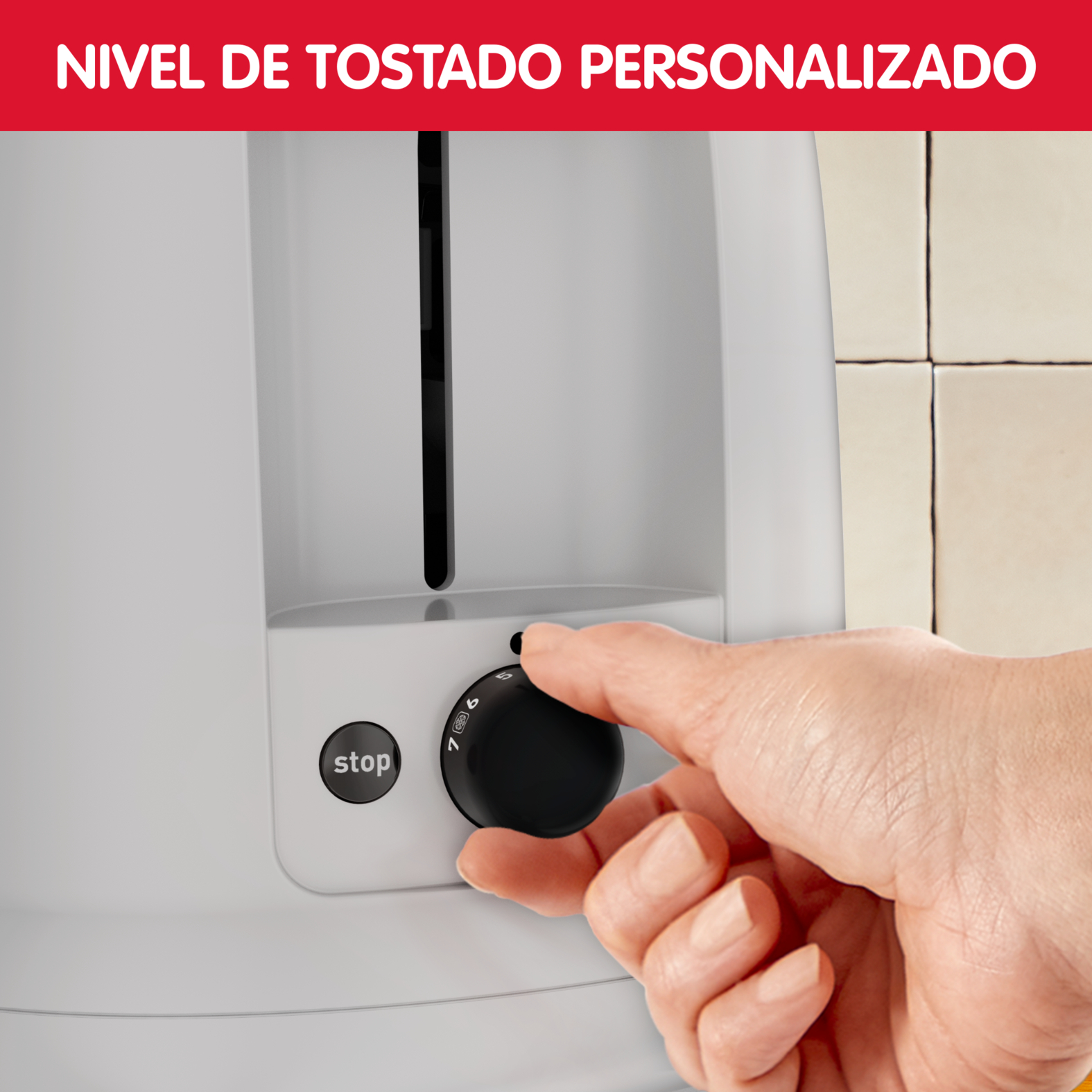 Una mano ajusta el dial de una tostadora blanca. El dial tiene números y un botón de parada. El fondo es una pared alicatada.